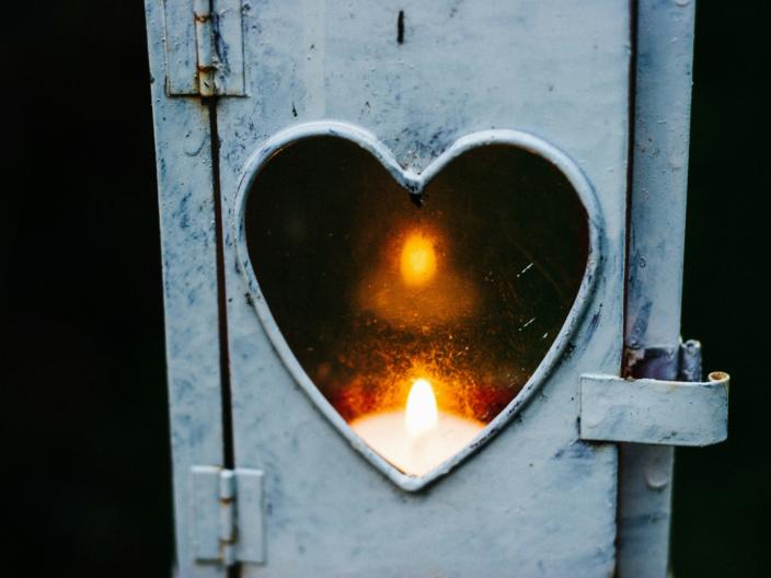 Ein Teelicht leuchtet in einer Laterne, deren Fenster ein kleines Herz ist
