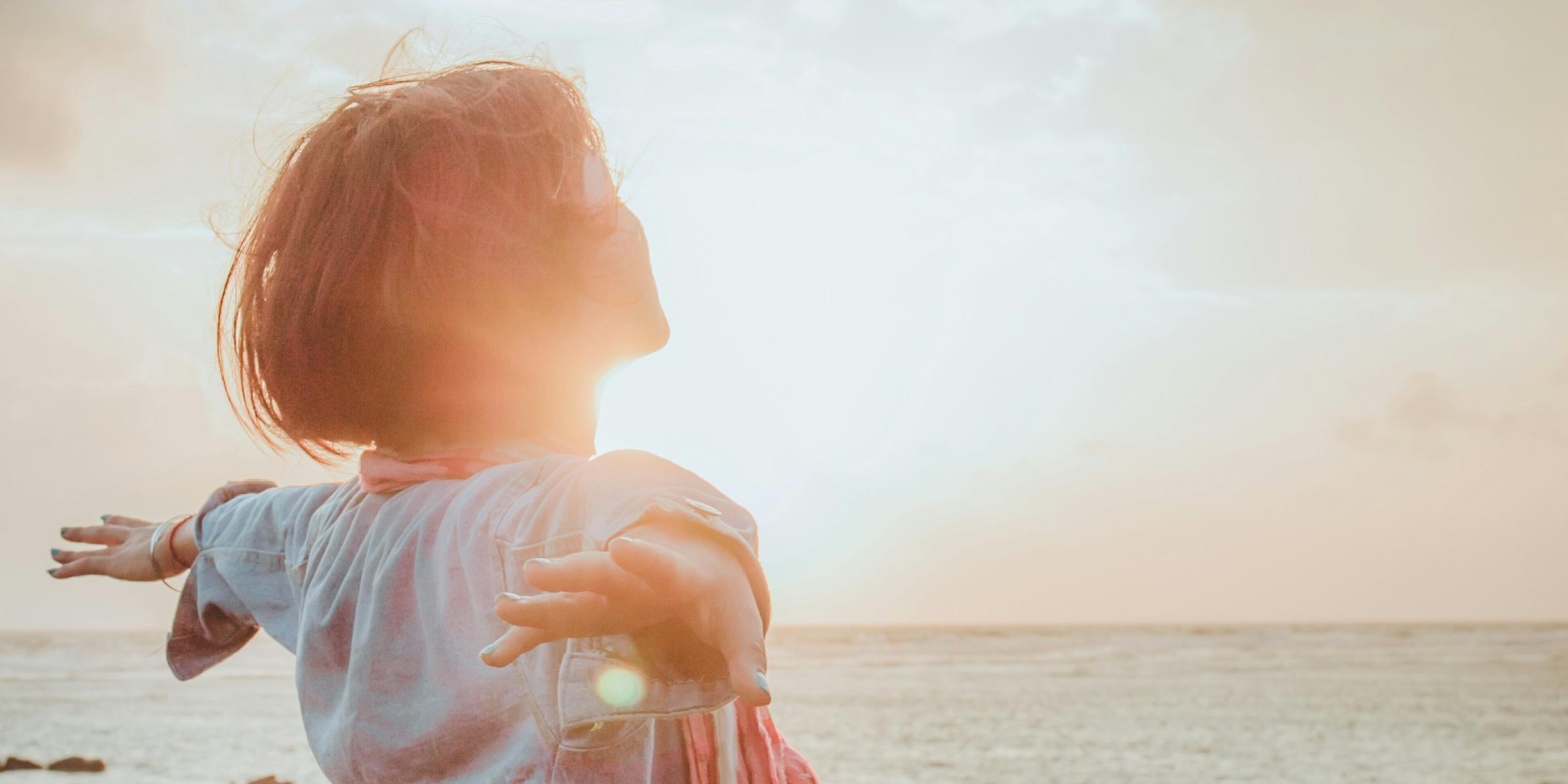 Eine Frau sitzt an einem steinigen Strand im Sonnenuntergang und wird von der Sonne bestrahlt