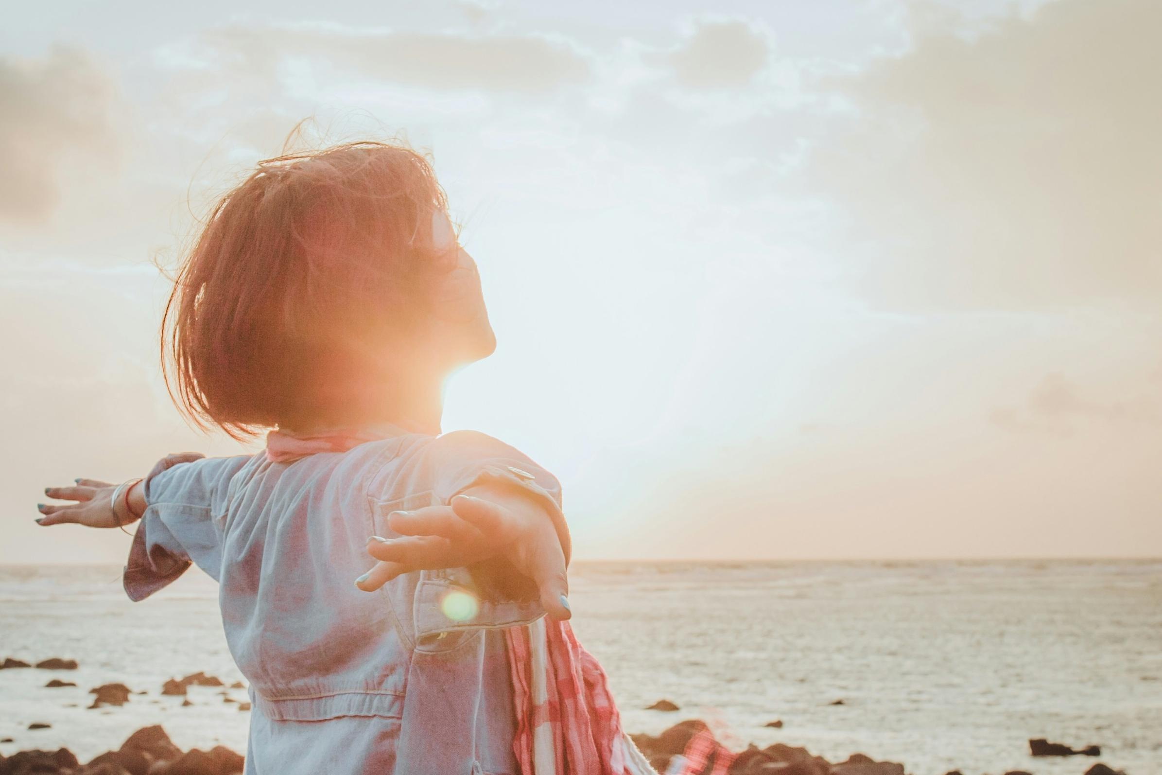 Eine Frau sitzt an einem steinigen Strand im Sonnenuntergang und wird von der Sonne bestrahlt