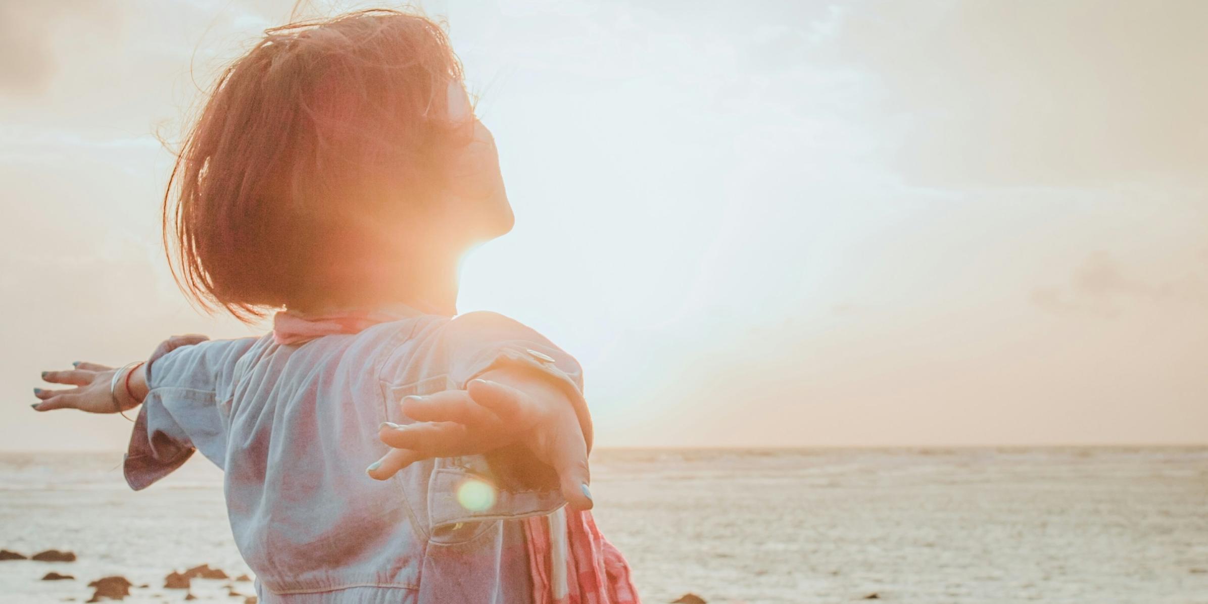 Eine Frau sitzt an einem steinigen Strand im Sonnenuntergang und wird von der Sonne bestrahlt