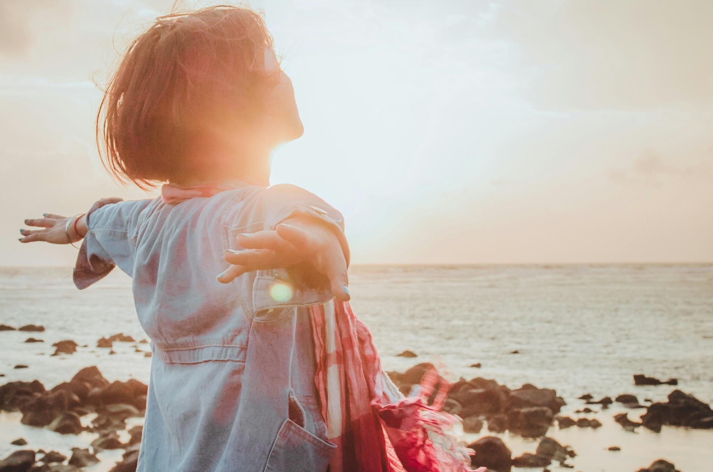 Eine Frau sitzt an einem steinigen Strand im Sonnenuntergang und wird von der Sonne bestrahlt