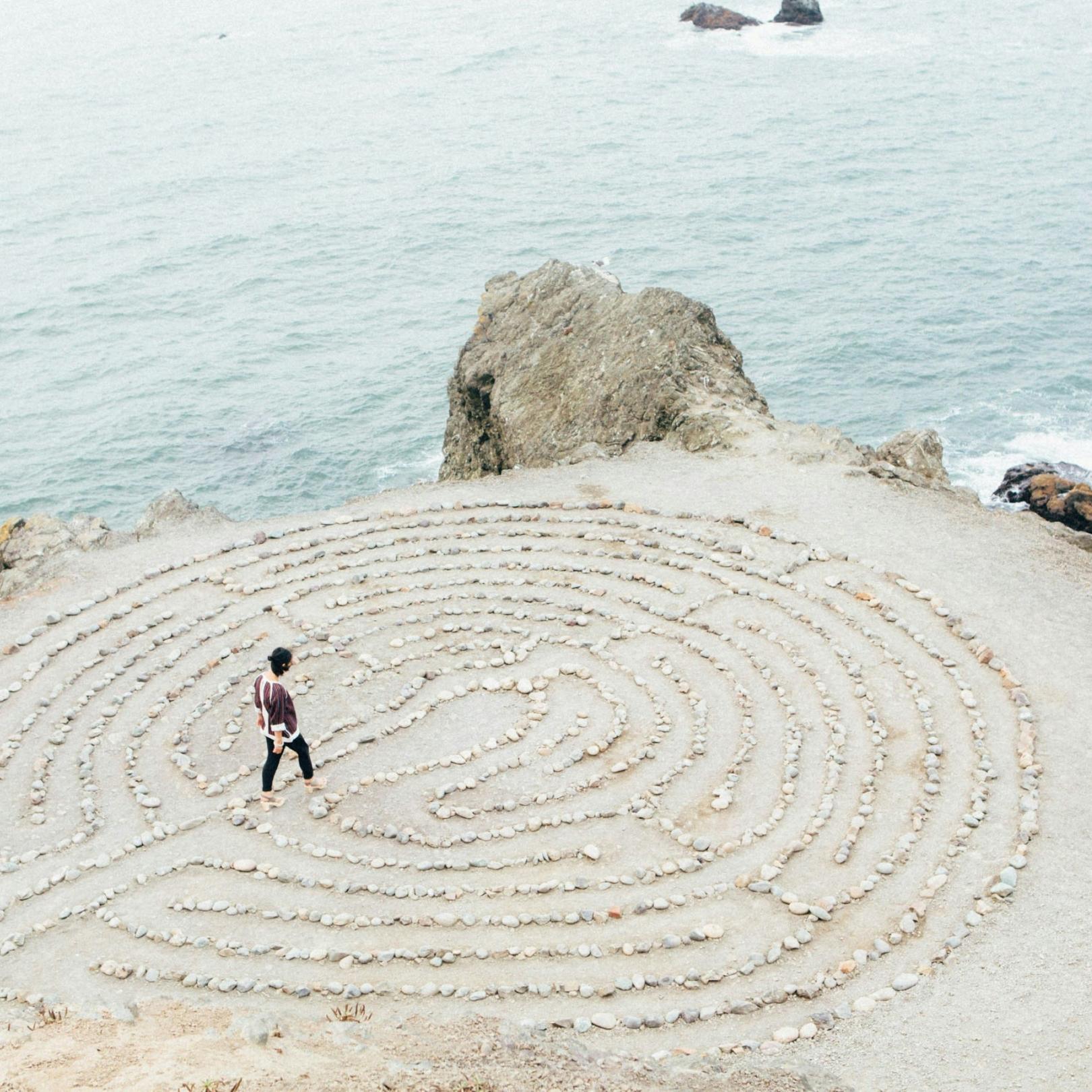 Eine Frau geht durch ein kreisförmiges Labyrinth am Strand, welches aus Steinen gelegt wurde