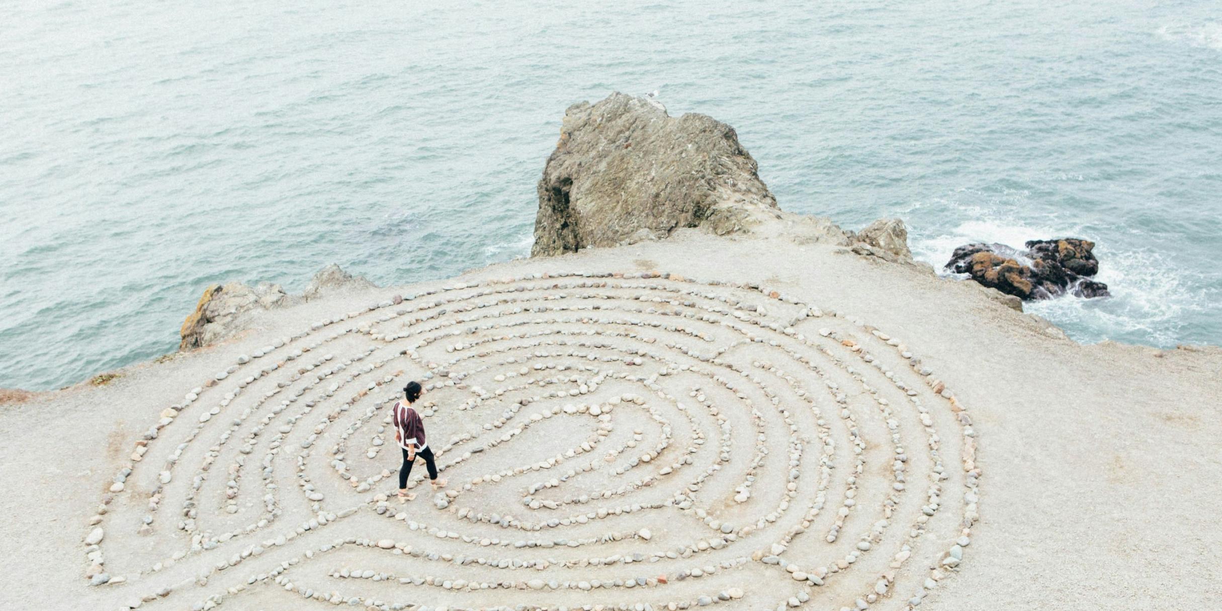 Eine Frau geht durch ein kreisförmiges Labyrinth am Strand, welches aus Steinen gelegt wurde