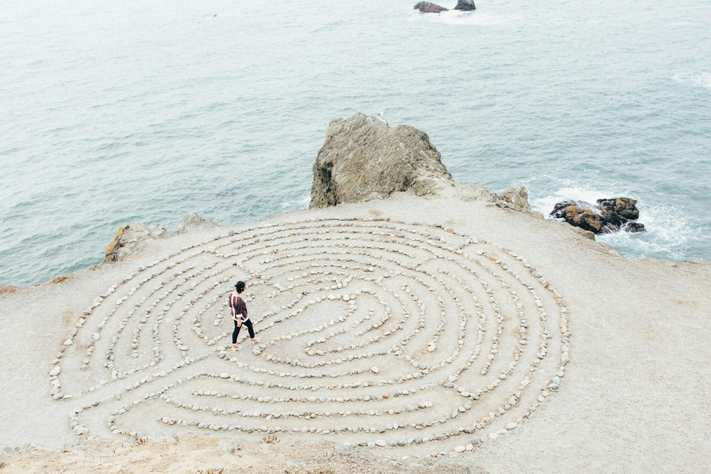 Eine Frau geht durch ein kreisförmiges Labyrinth am Strand, welches aus Steinen gelegt wurde