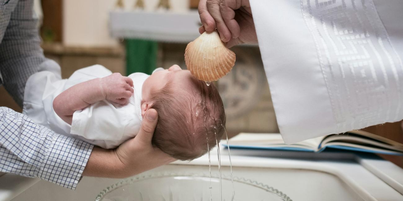 Ein kleines Kind wird über ein Taufbecken gehalten und empfängt die Taufe mit Taufwasser