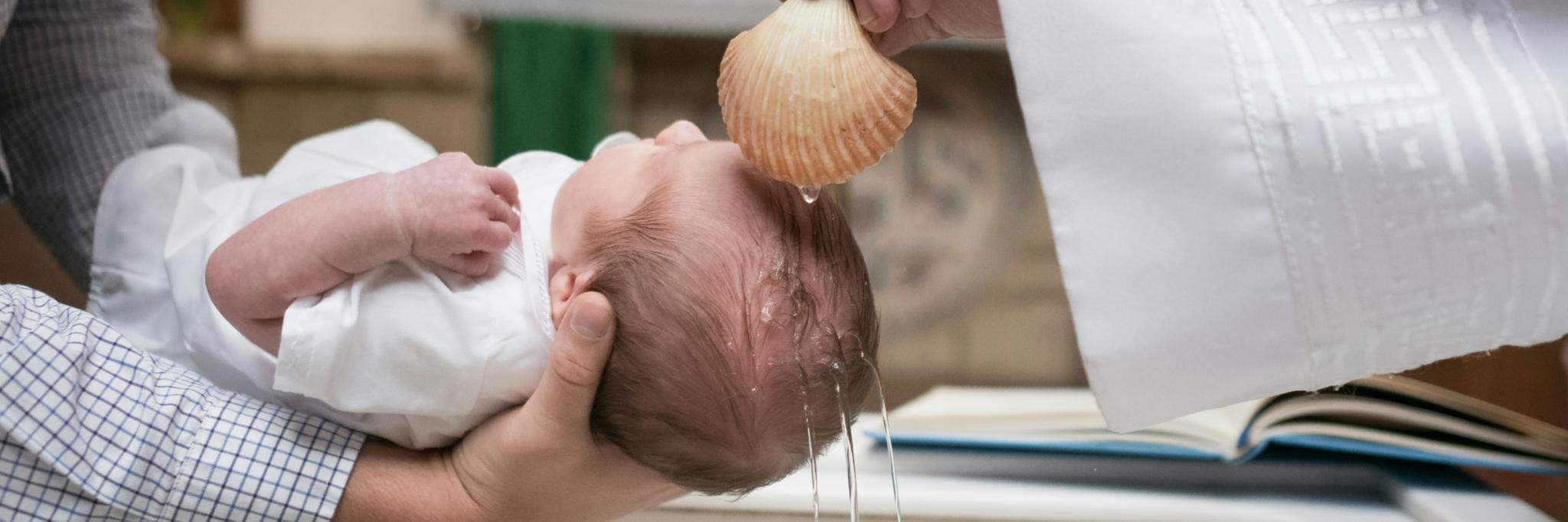 Ein kleines Kind wird über ein Taufbecken gehalten und empfängt die Taufe mit Taufwasser