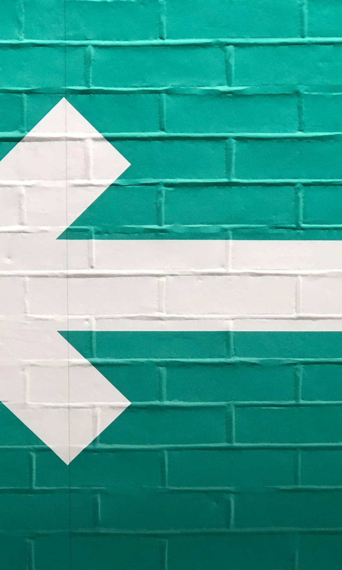 Foto einer grün gestrichenen Wand auf der ein dicker weißer Pfeil nach links zeigt