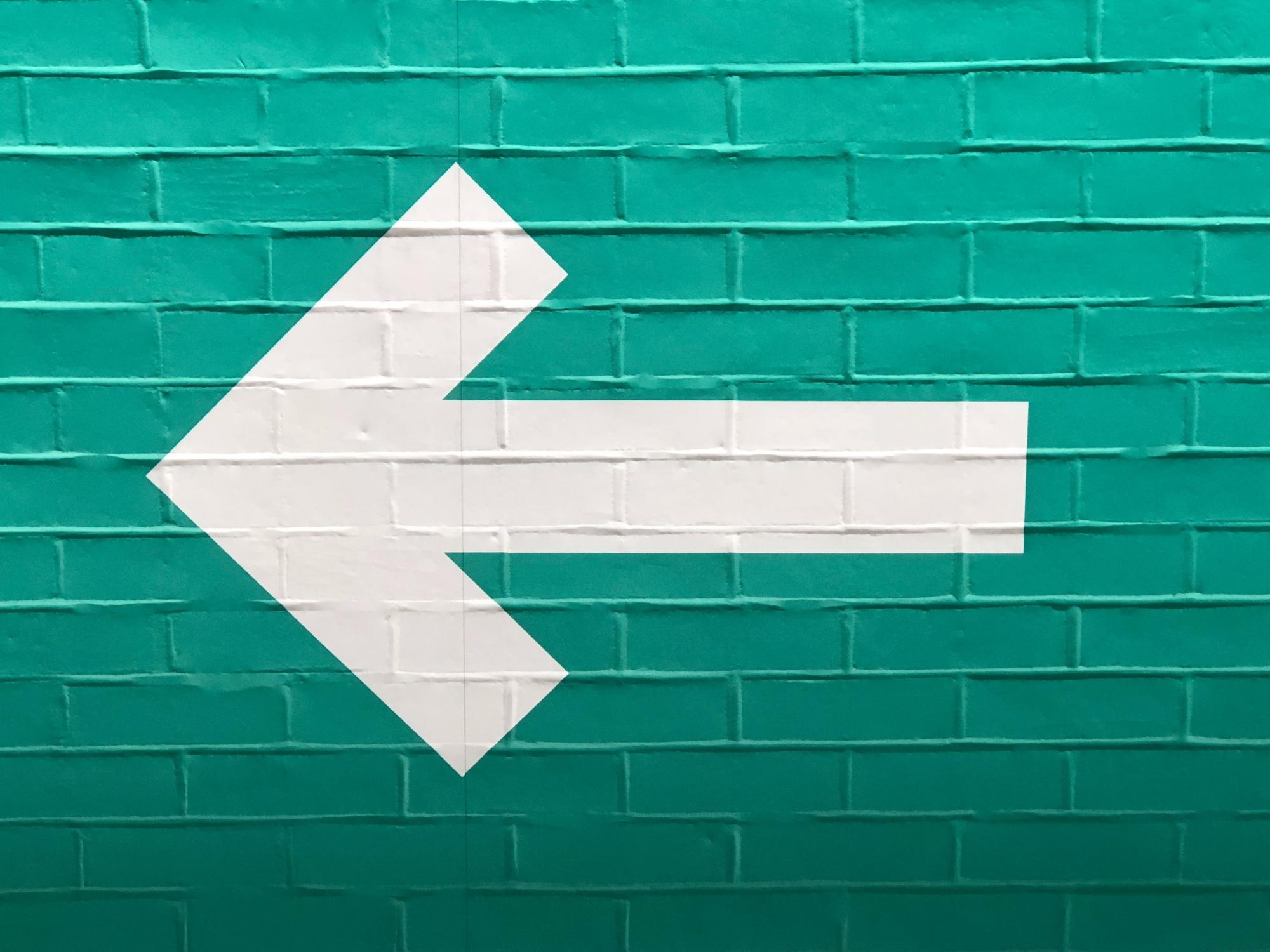 Foto einer grün gestrichenen Wand auf der ein dicker weißer Pfeil nach links zeigt