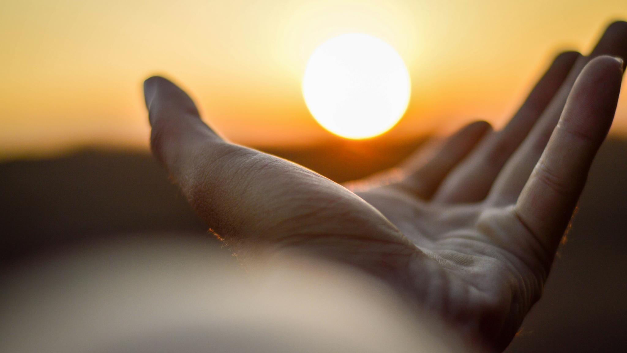 Eine Hand ist mit der Handfläche nach oben zu sehen und es sieht so aus, als würde diese Hand die untergehende Sonne halten