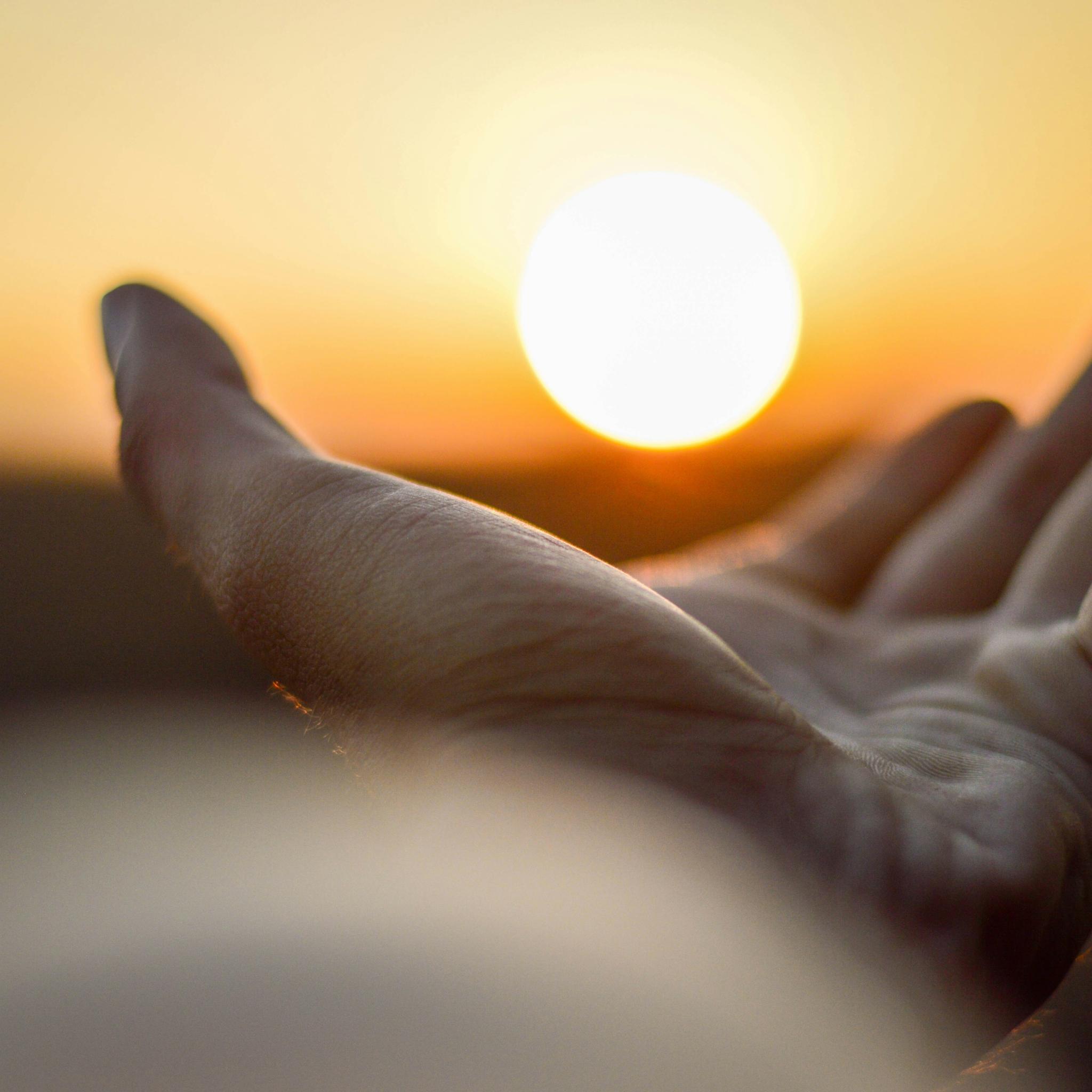 Eine Hand ist mit der Handfläche nach oben zu sehen und es sieht so aus, als würde diese Hand die untergehende Sonne halten