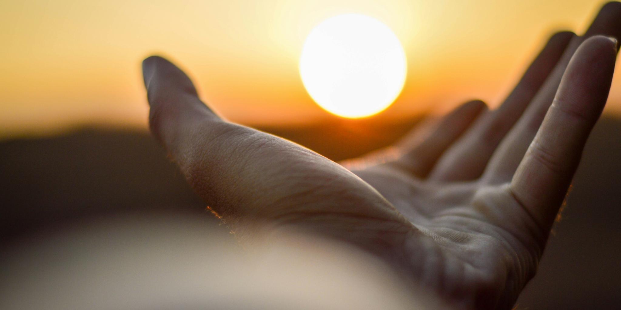 Eine Hand ist mit der Handfläche nach oben zu sehen und es sieht so aus, als würde diese Hand die untergehende Sonne halten