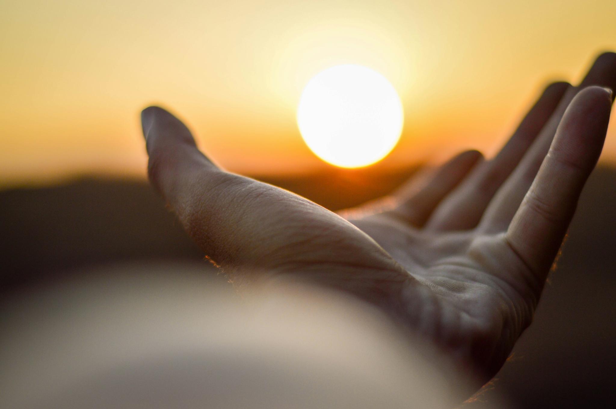 Eine Hand ist mit der Handfläche nach oben zu sehen und es sieht so aus, als würde diese Hand die untergehende Sonne halten