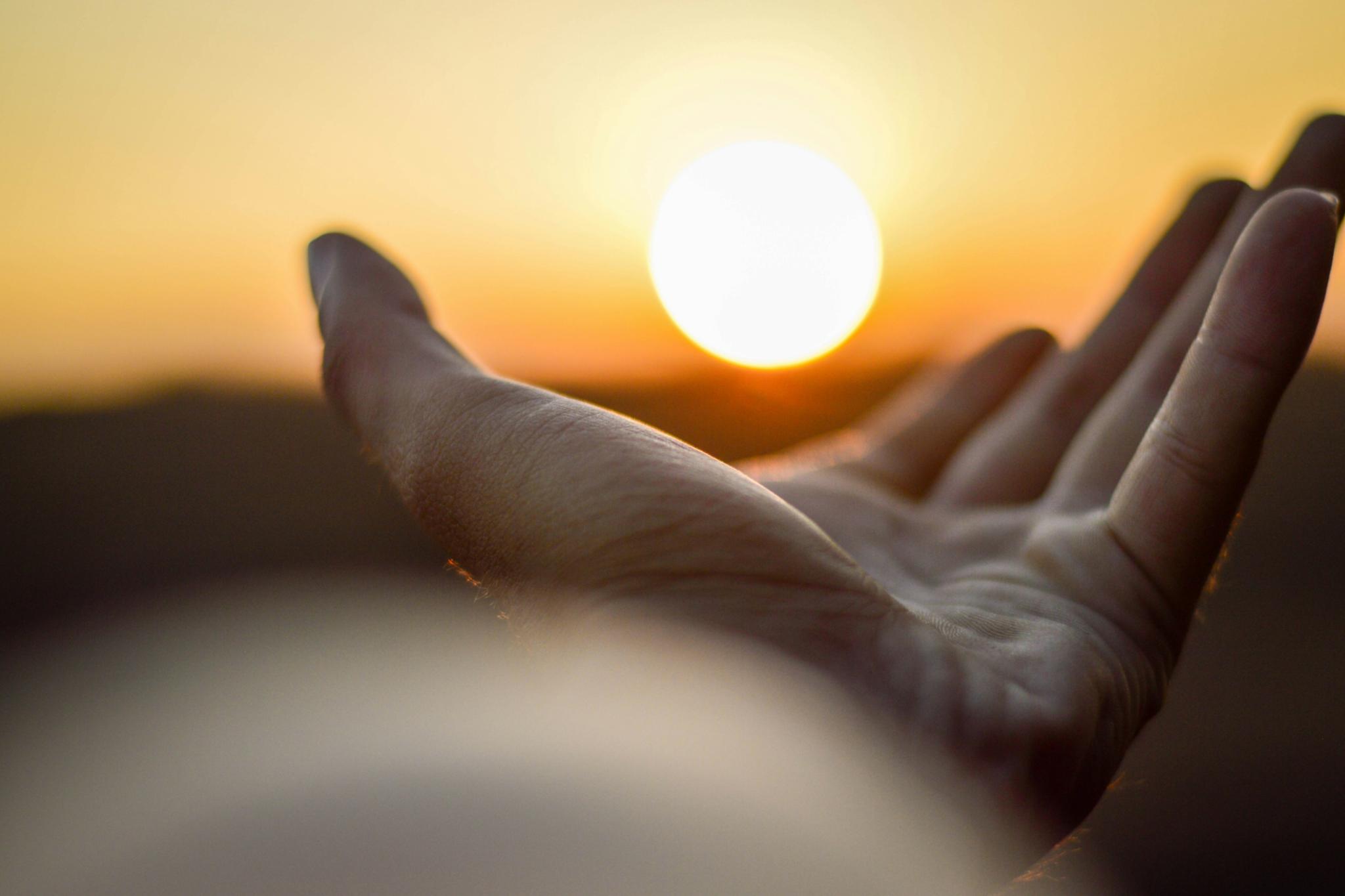 Eine Hand ist mit der Handfläche nach oben zu sehen und es sieht so aus, als würde diese Hand die untergehende Sonne halten