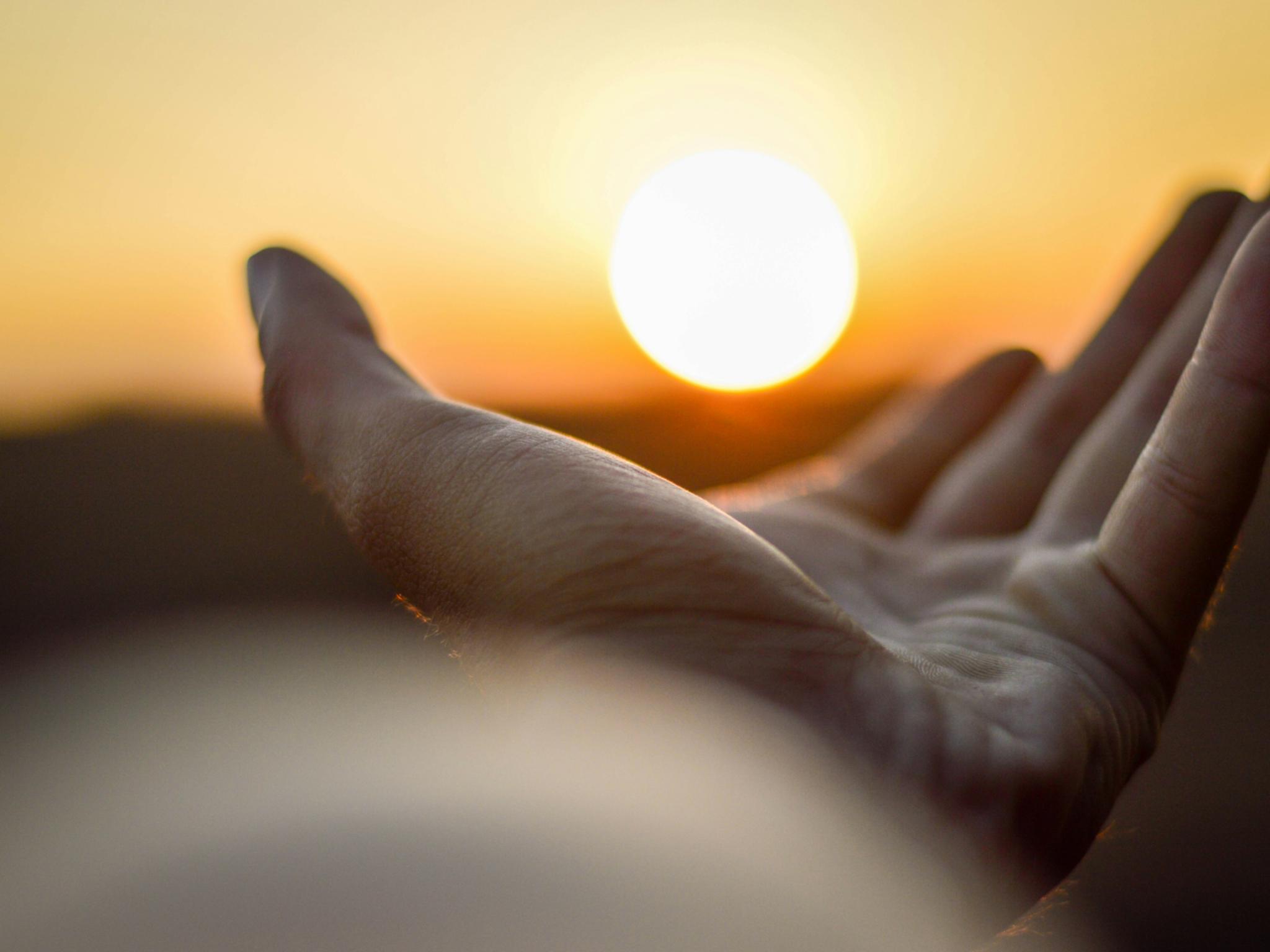 Eine Hand ist mit der Handfläche nach oben zu sehen und es sieht so aus, als würde diese Hand die untergehende Sonne halten