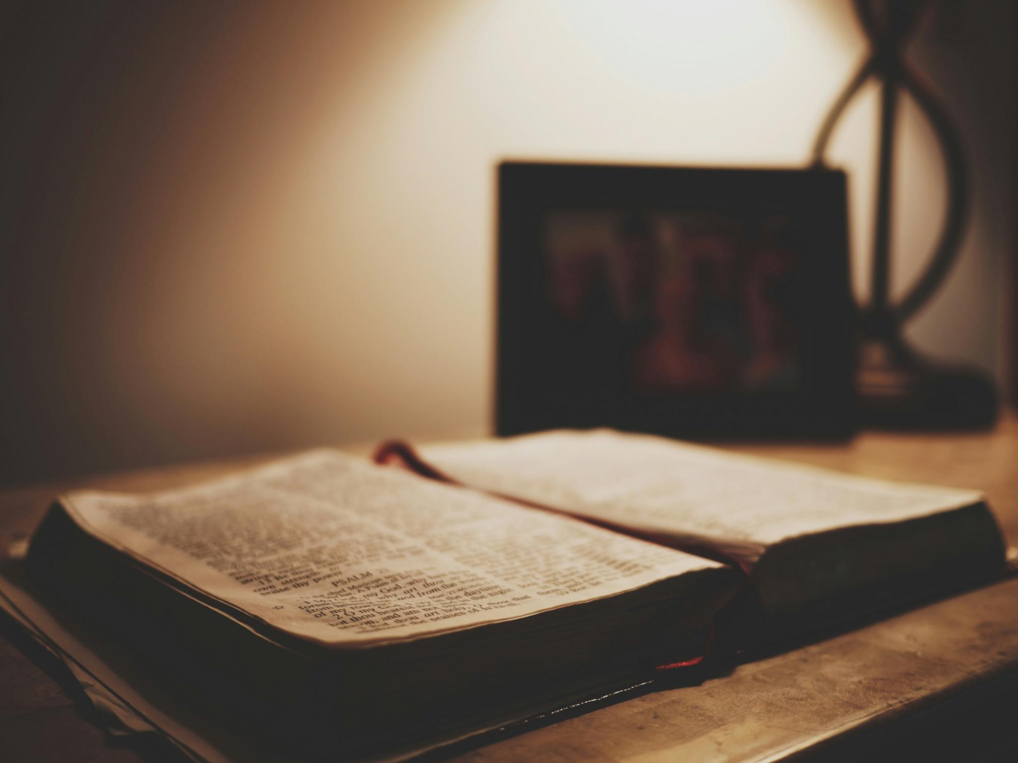 Eine aufgeschlagene alte Bibel liegt auf einem Schreibtisch. Der Raum ist nur schwach beleuchtet