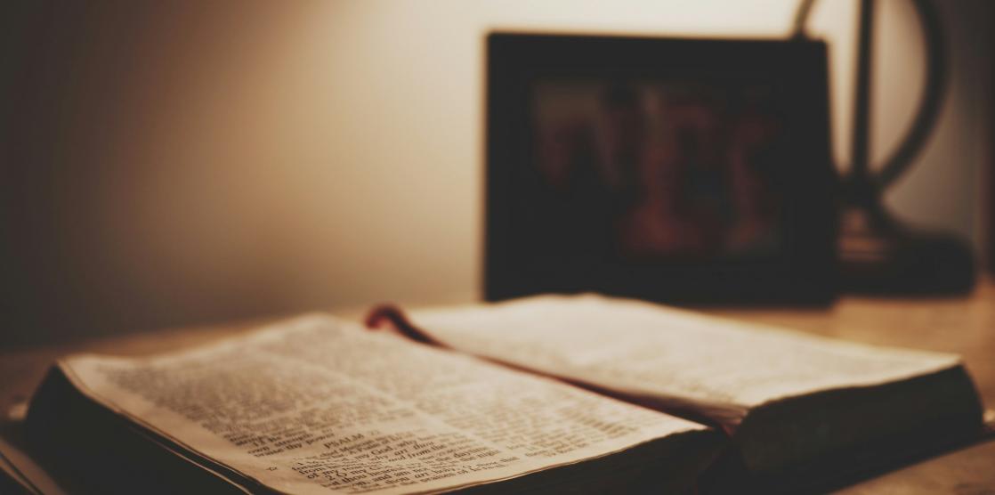 Eine aufgeschlagene alte Bibel liegt auf einem Schreibtisch. Der Raum ist nur schwach beleuchtet