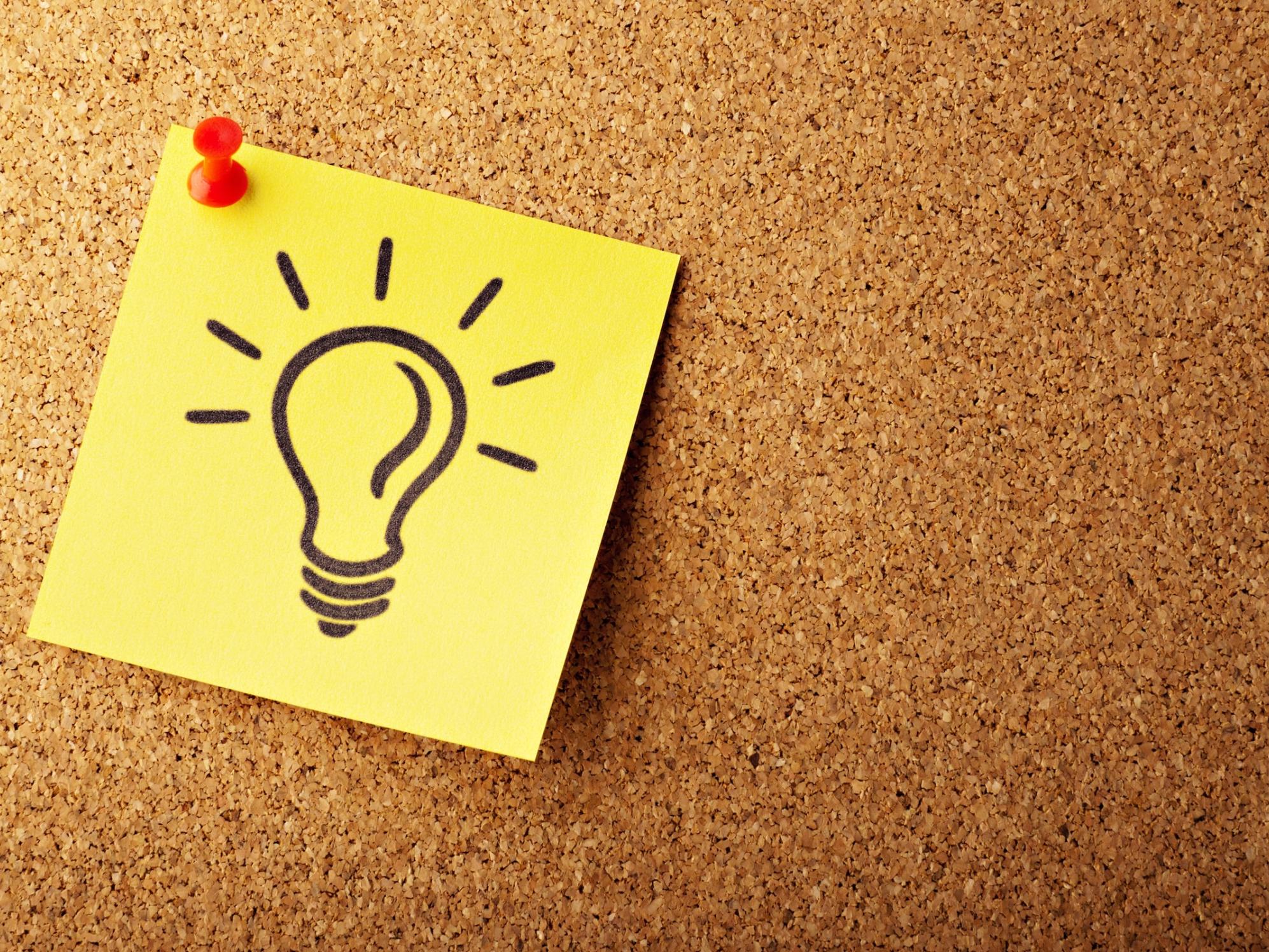 An einer Pinnwand ist ein gelber Zettel auf dem eine Glühbirne abgebildet ist, angepinnt.