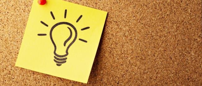 An einer Pinnwand ist ein gelber Zettel auf dem eine Glühbirne abgebildet ist, angepinnt.