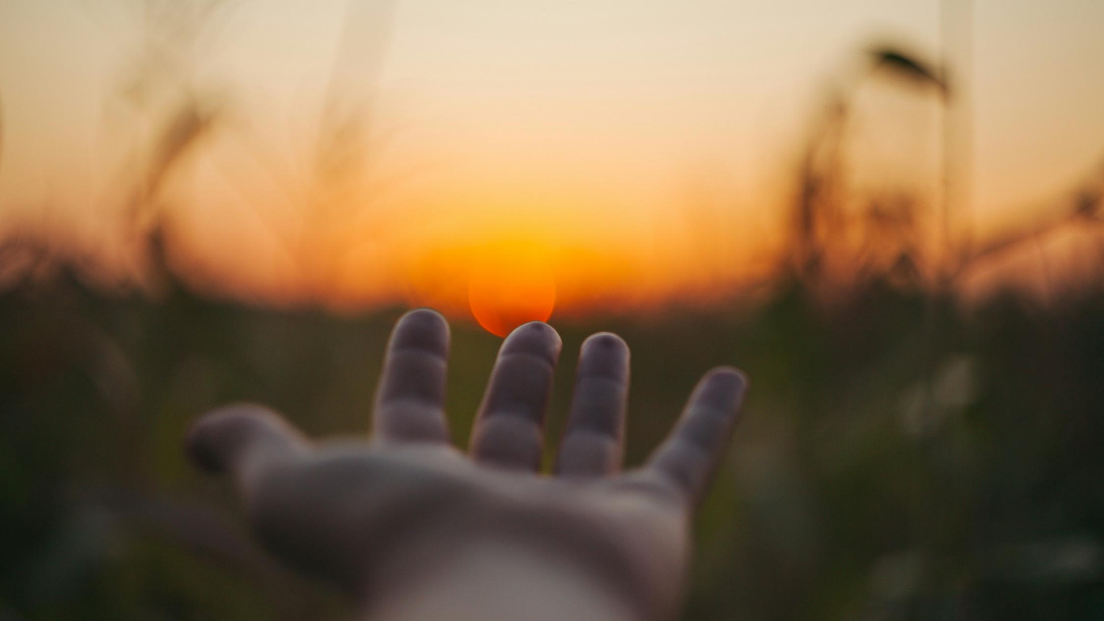 Eine Hand wird Richtung Sonnenuntergang ausgestreckt