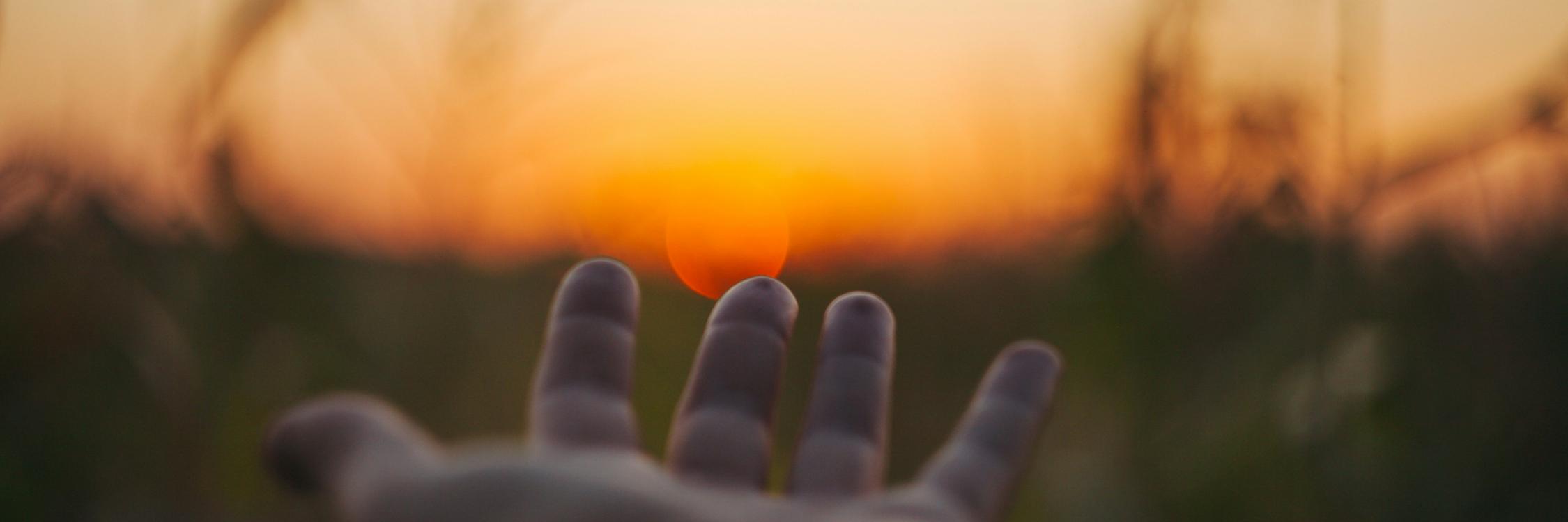 Eine Hand wird Richtung Sonnenuntergang ausgestreckt