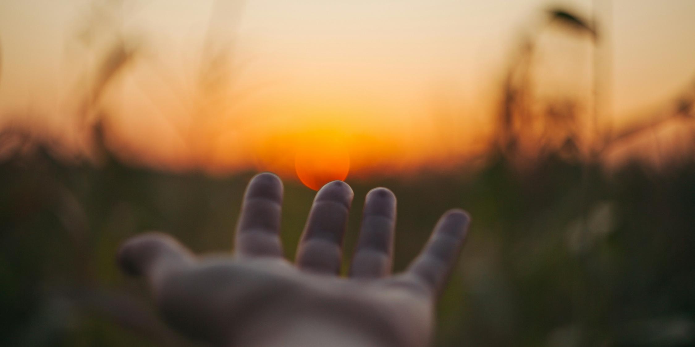 Eine Hand wird Richtung Sonnenuntergang ausgestreckt