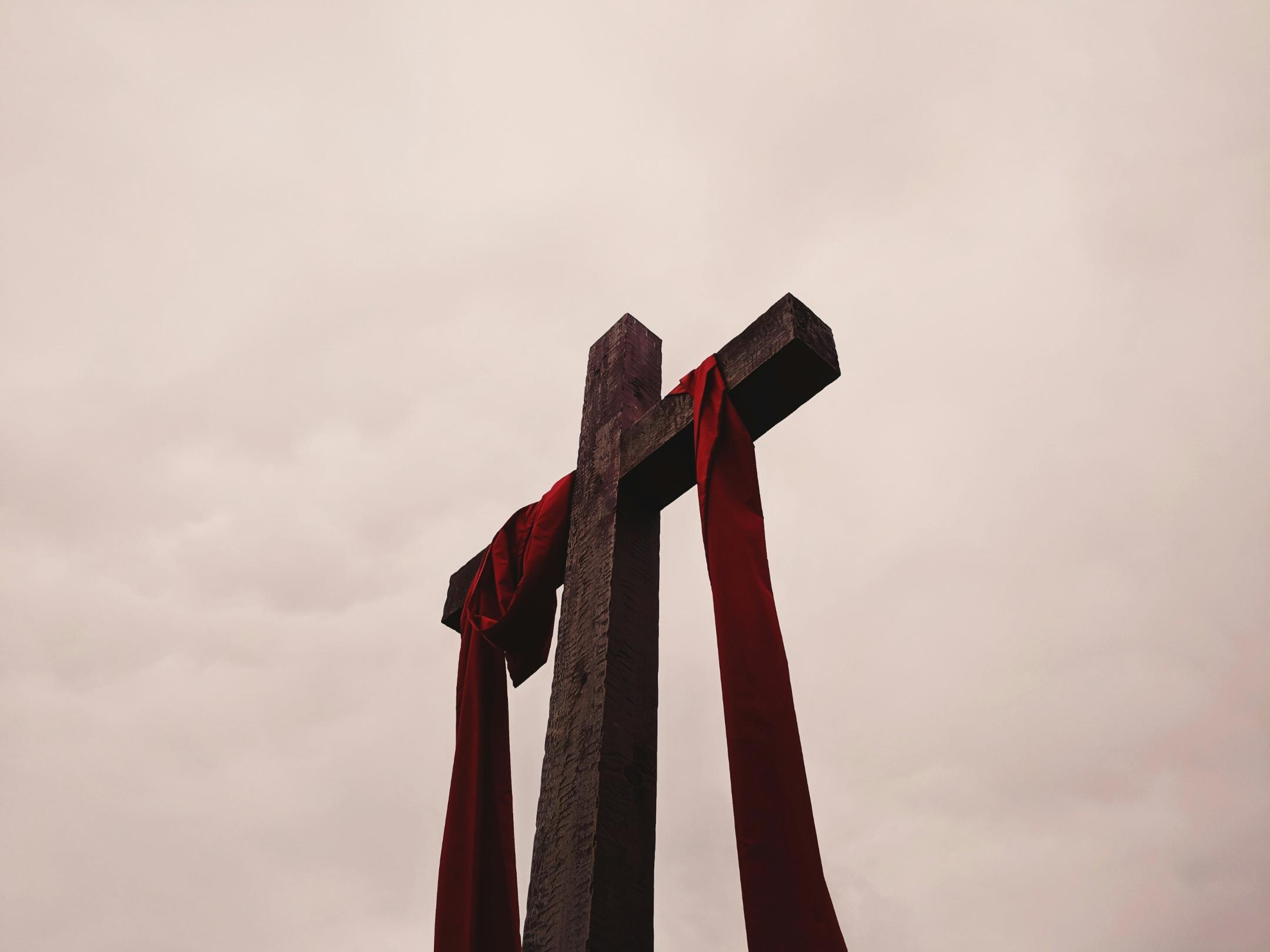 Man sieht ein großes Kreuz aus Holz, auf dem ein rotes Tuch liegt