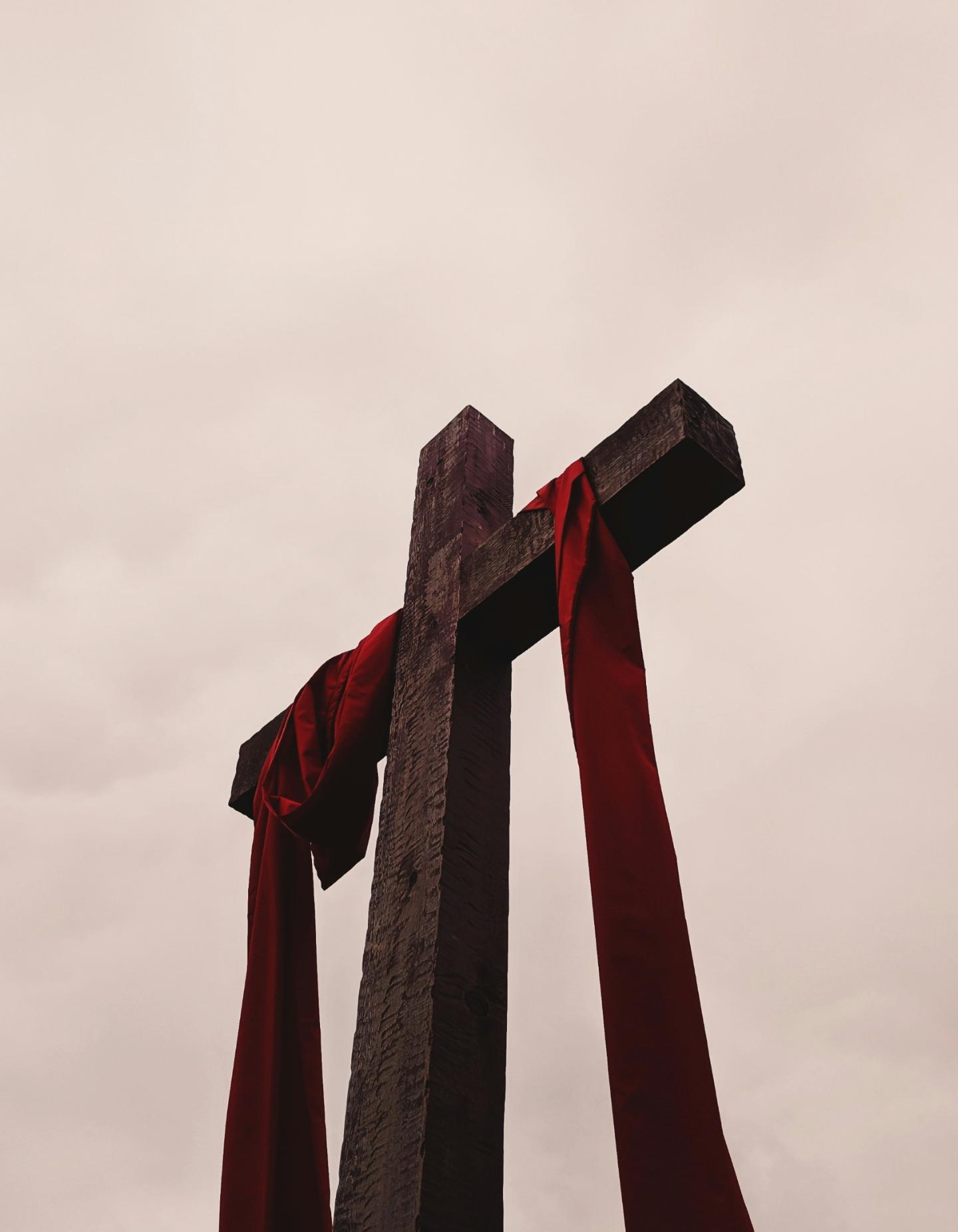 Man sieht ein großes Kreuz aus Holz, auf dem ein rotes Tuch liegt