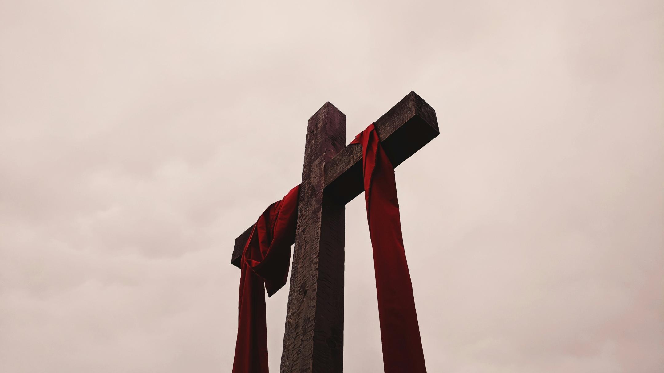 Man sieht ein großes Kreuz aus Holz, auf dem ein rotes Tuch liegt