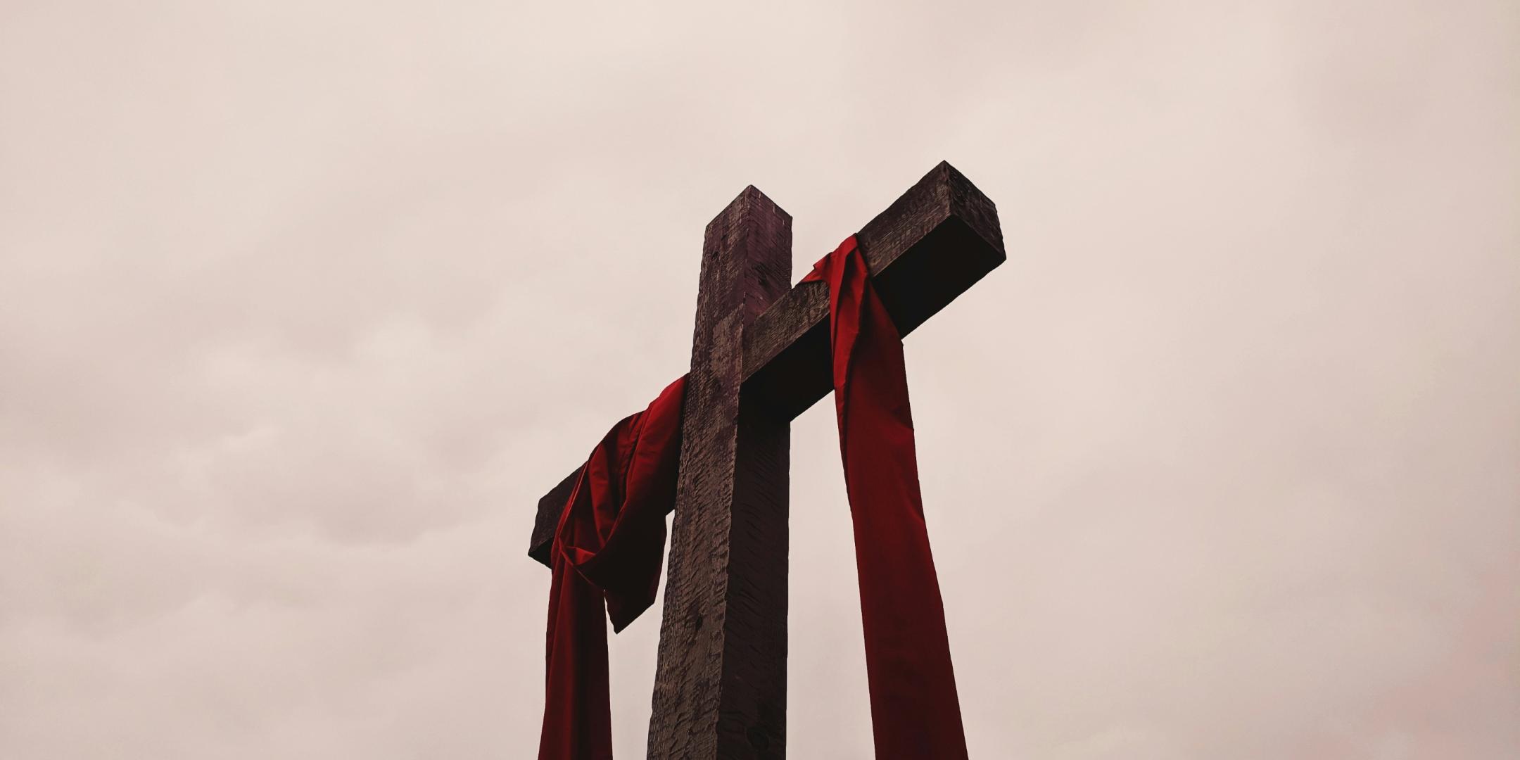 Man sieht ein großes Kreuz aus Holz, auf dem ein rotes Tuch liegt