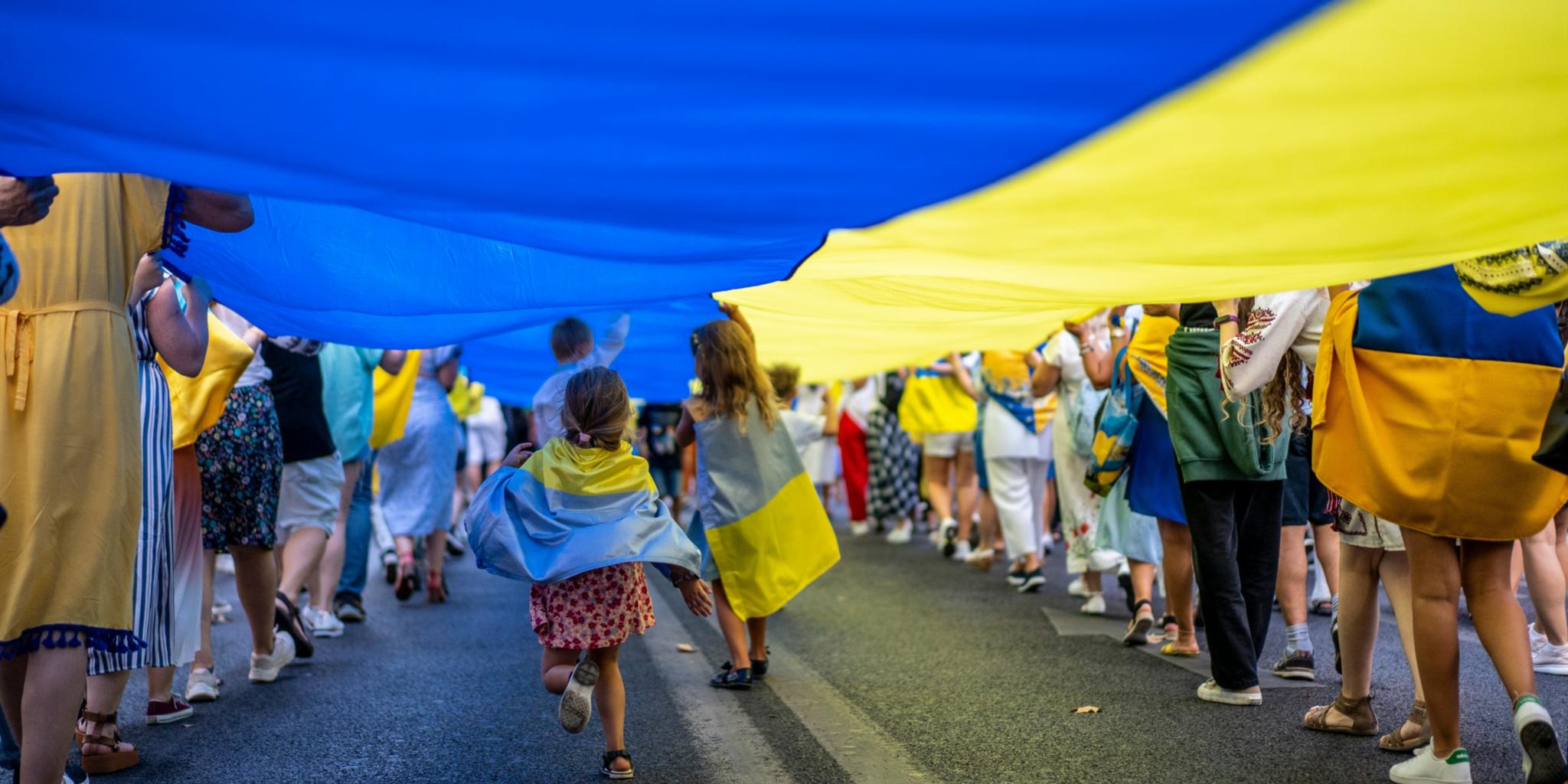Kinder laufen unter einer riesigen ukrainischen Flagge