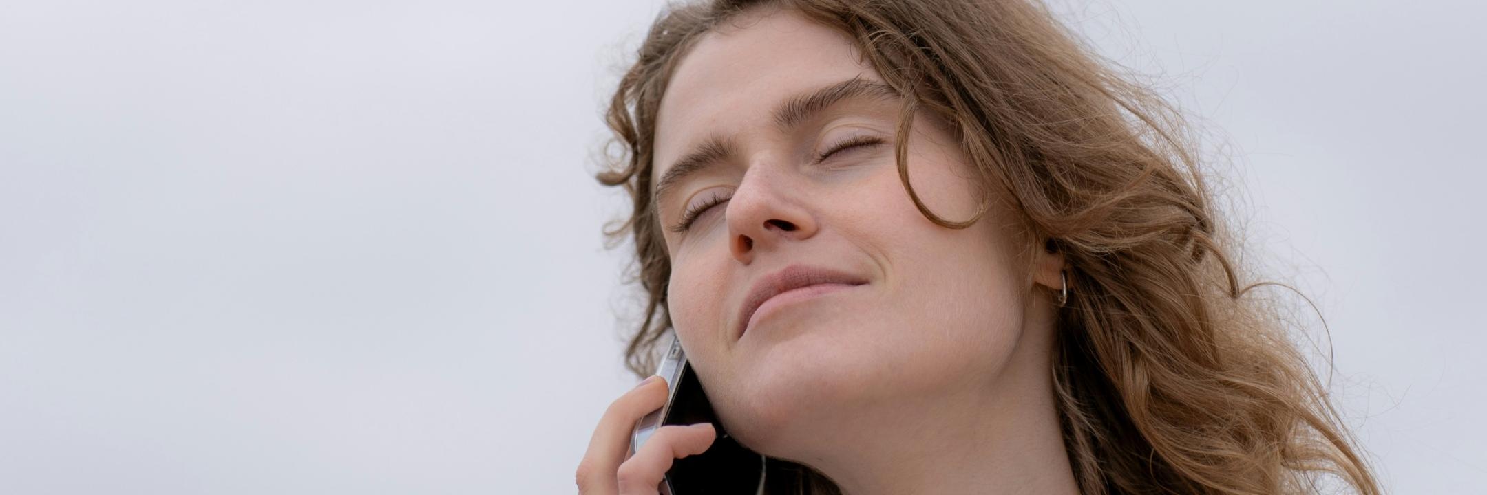 Eine junge Frau telefoniert mit geschlossenen Augen mit dem Handy