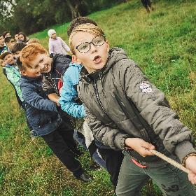 Über zehn Kinder im Grundschulalter stehen auf einer Wiese und ziehen mit allen Kräften an einem dicken Seil