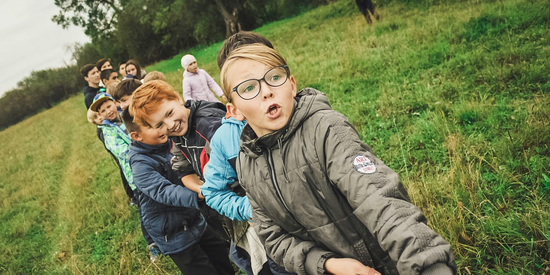 Über zehn Kinder im Grundschulalter stehen auf einer Wiese und ziehen mit allen Kräften an einem dicken Seil