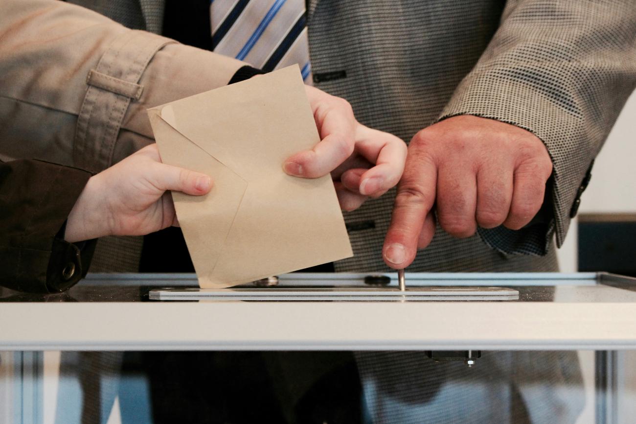 Hände werfen einen Umschlag in eine Wahlurne