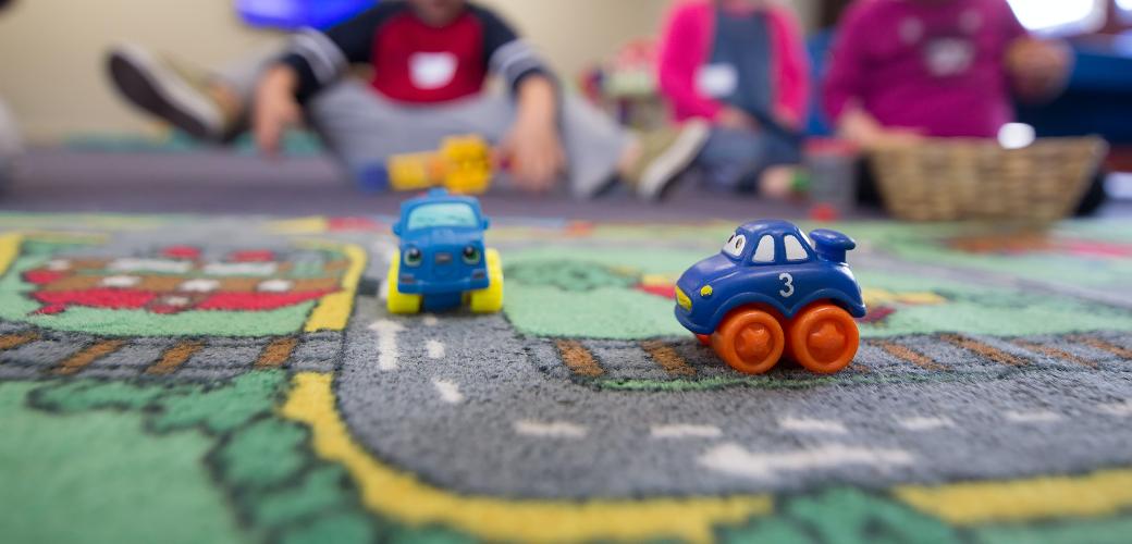 Auf einem Spielteppich stehen zwei kleine Spielzeugautos.