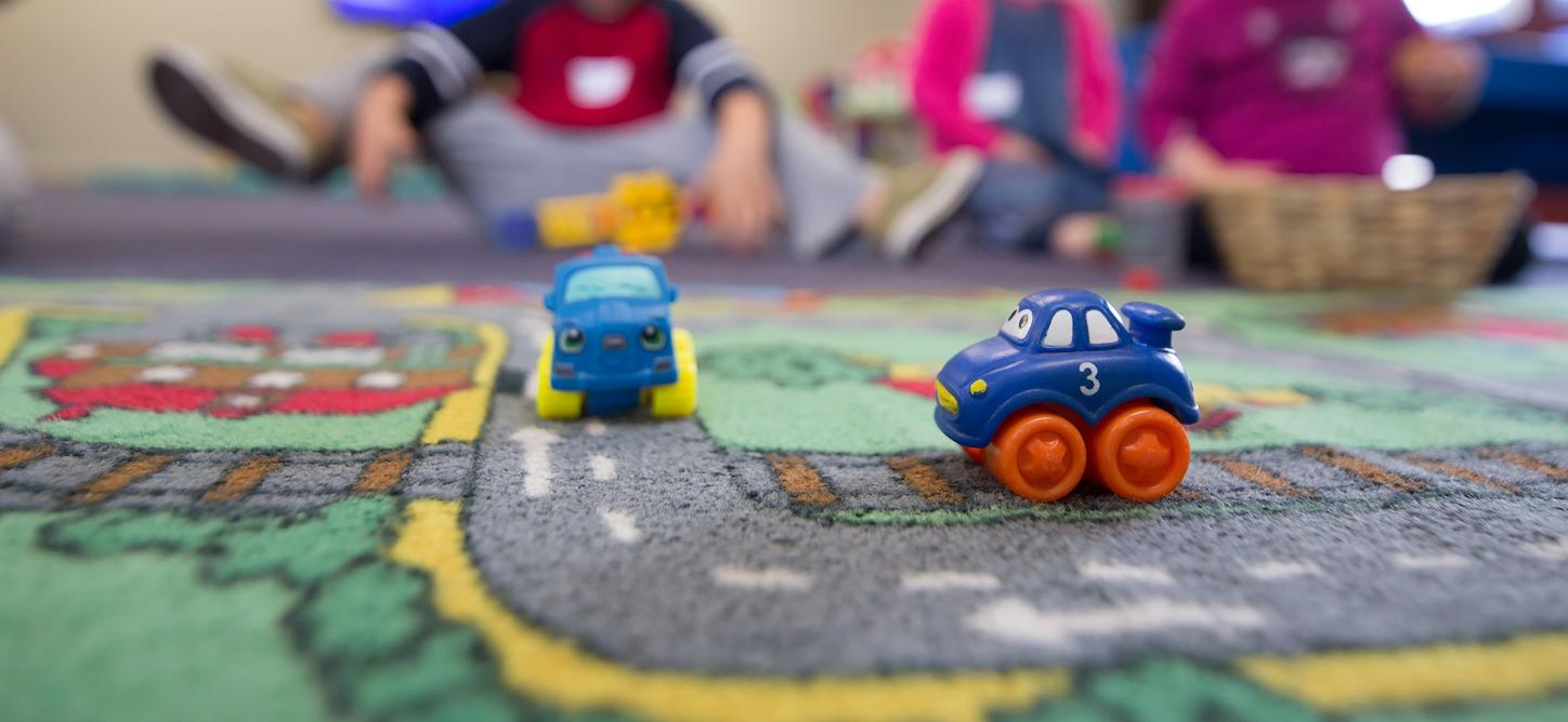 Auf einem Spielteppich stehen zwei kleine Spielzeugautos.