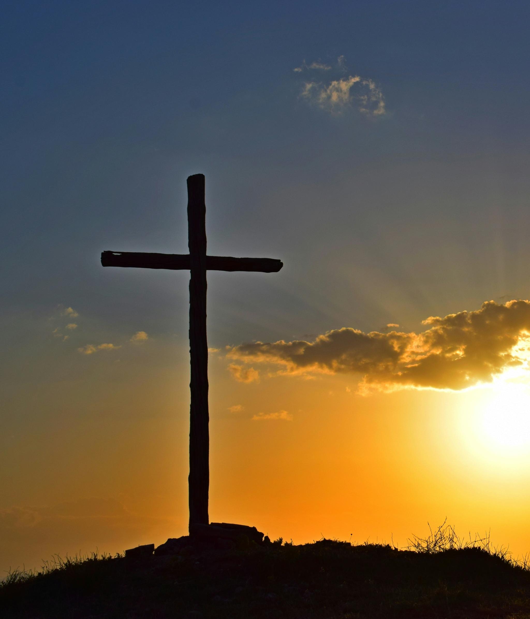 Auf einem Berg steht ein großes Kreuz, dahinter geht die Sonne unter