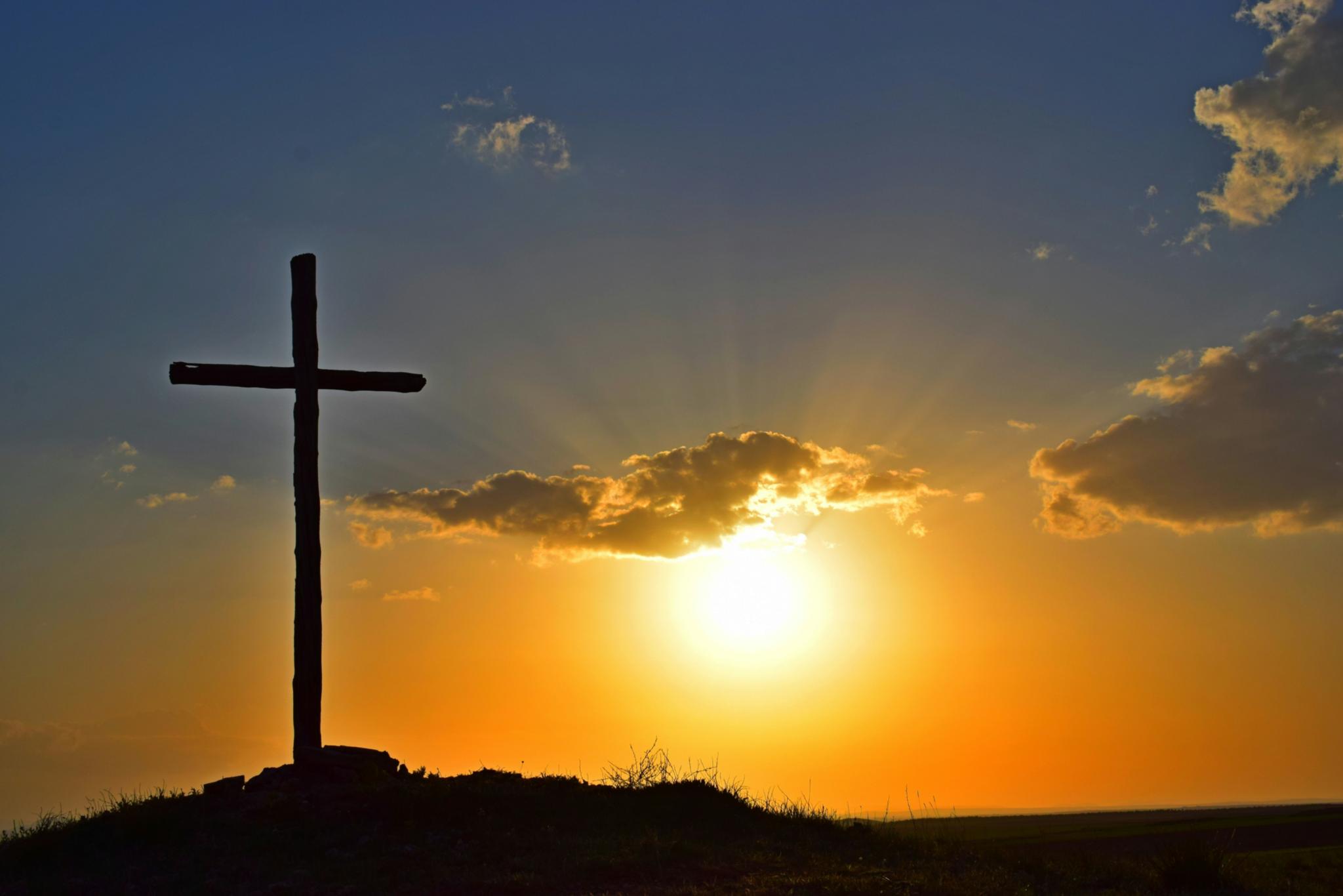 Auf einem Berg steht ein großes Kreuz, dahinter geht die Sonne unter