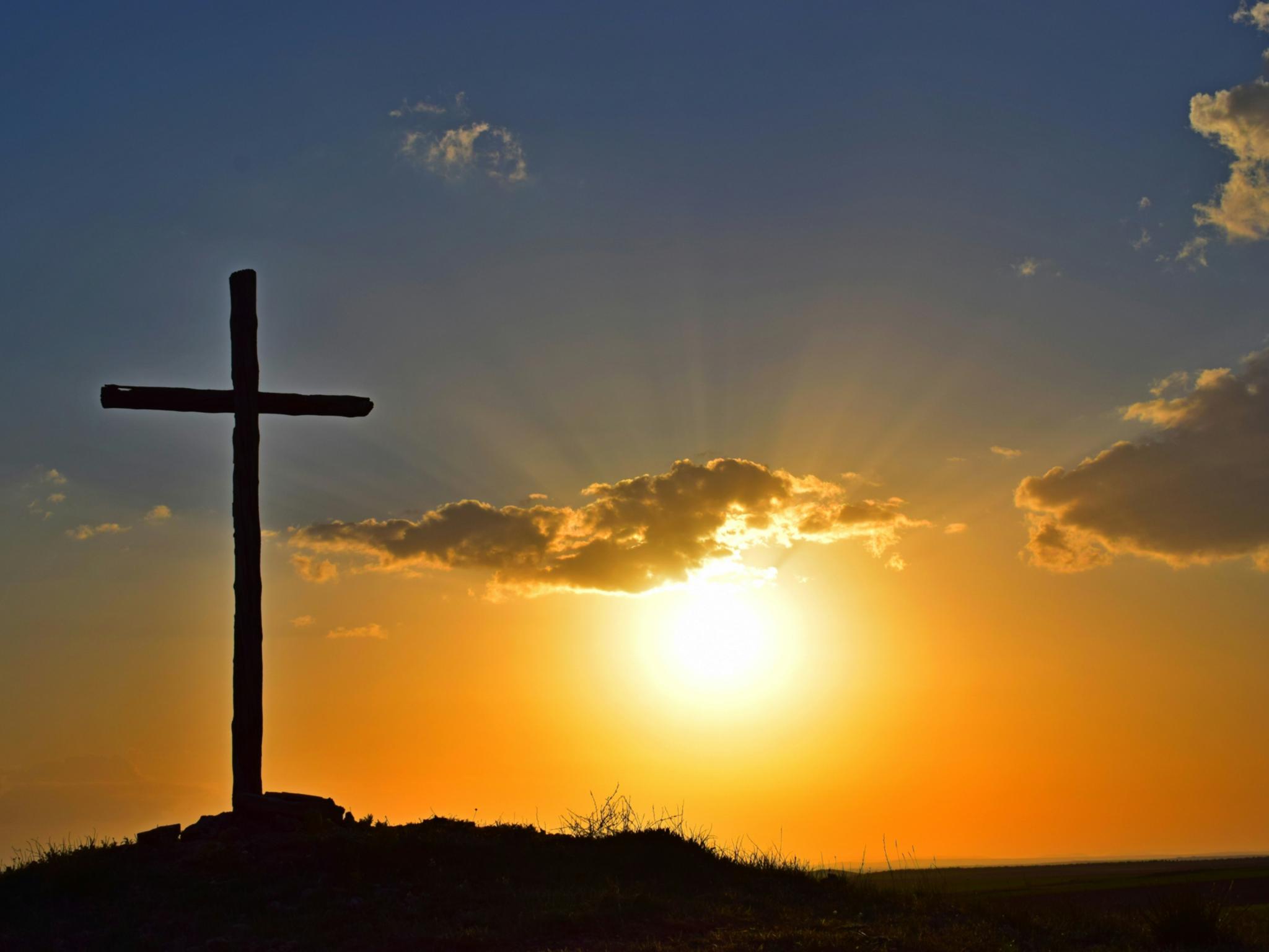 Auf einem Berg steht ein großes Kreuz, dahinter geht die Sonne unter