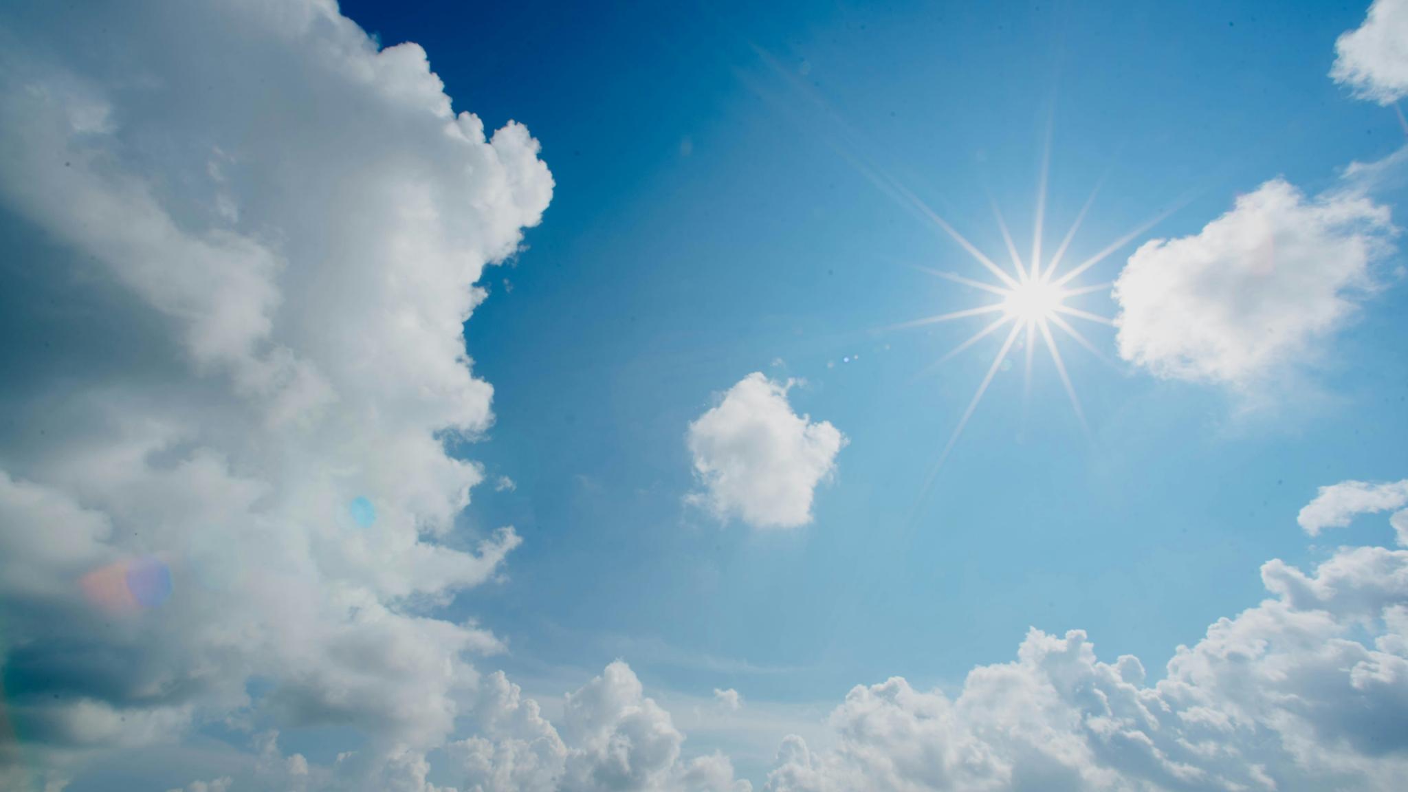 Die Sonne scheint am blauen Himmel. Rundherum sind weiße Wolken