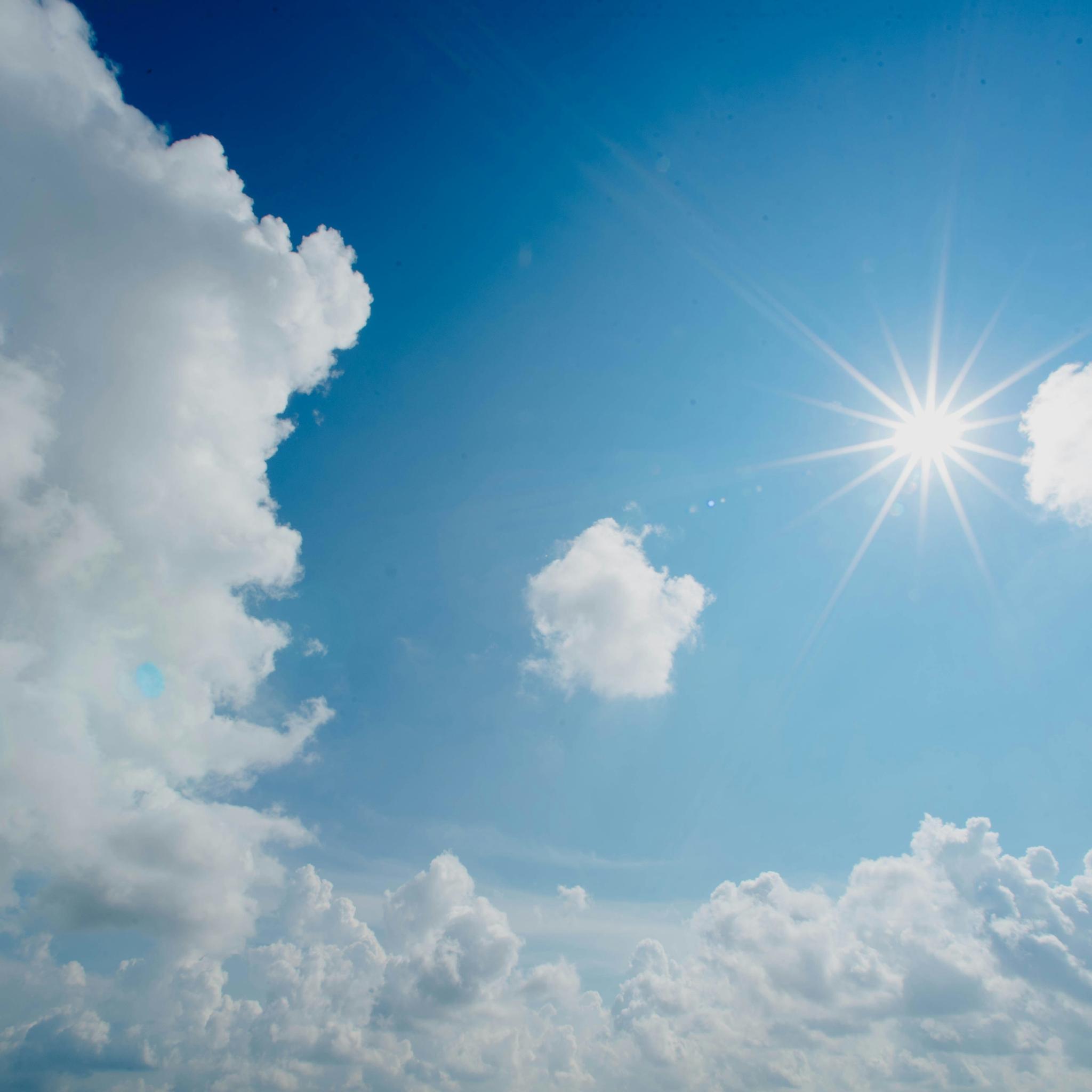 Die Sonne scheint am blauen Himmel. Rundherum sind weiße Wolken