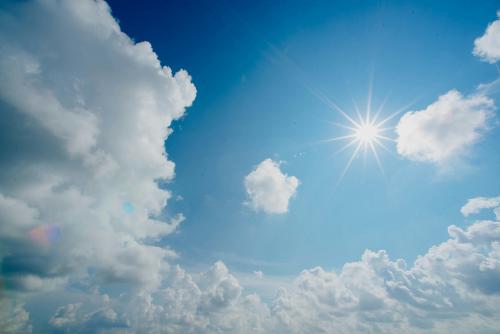Die Sonne scheint am blauen Himmel. Rundherum sind weiße Wolken
