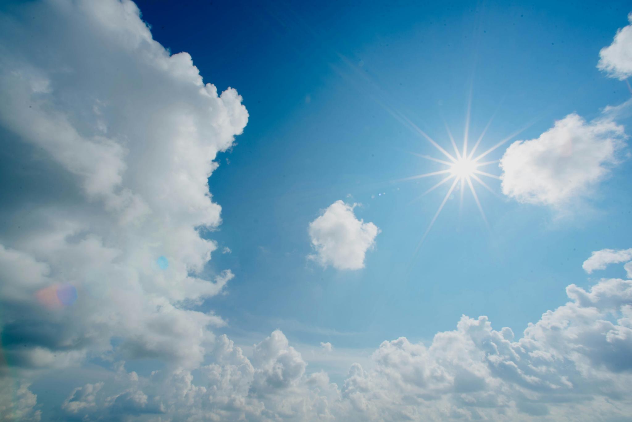 Die Sonne scheint am blauen Himmel. Rundherum sind weiße Wolken