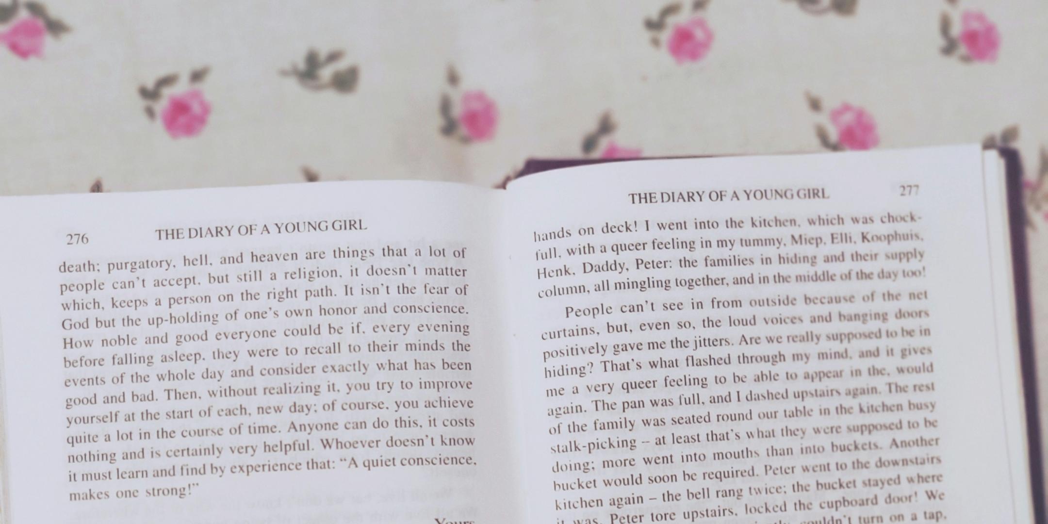 Auf einem Tisch mit Blumendecke liegt das geöffnete Tagebuch der Anne Frank in englischer Sprache