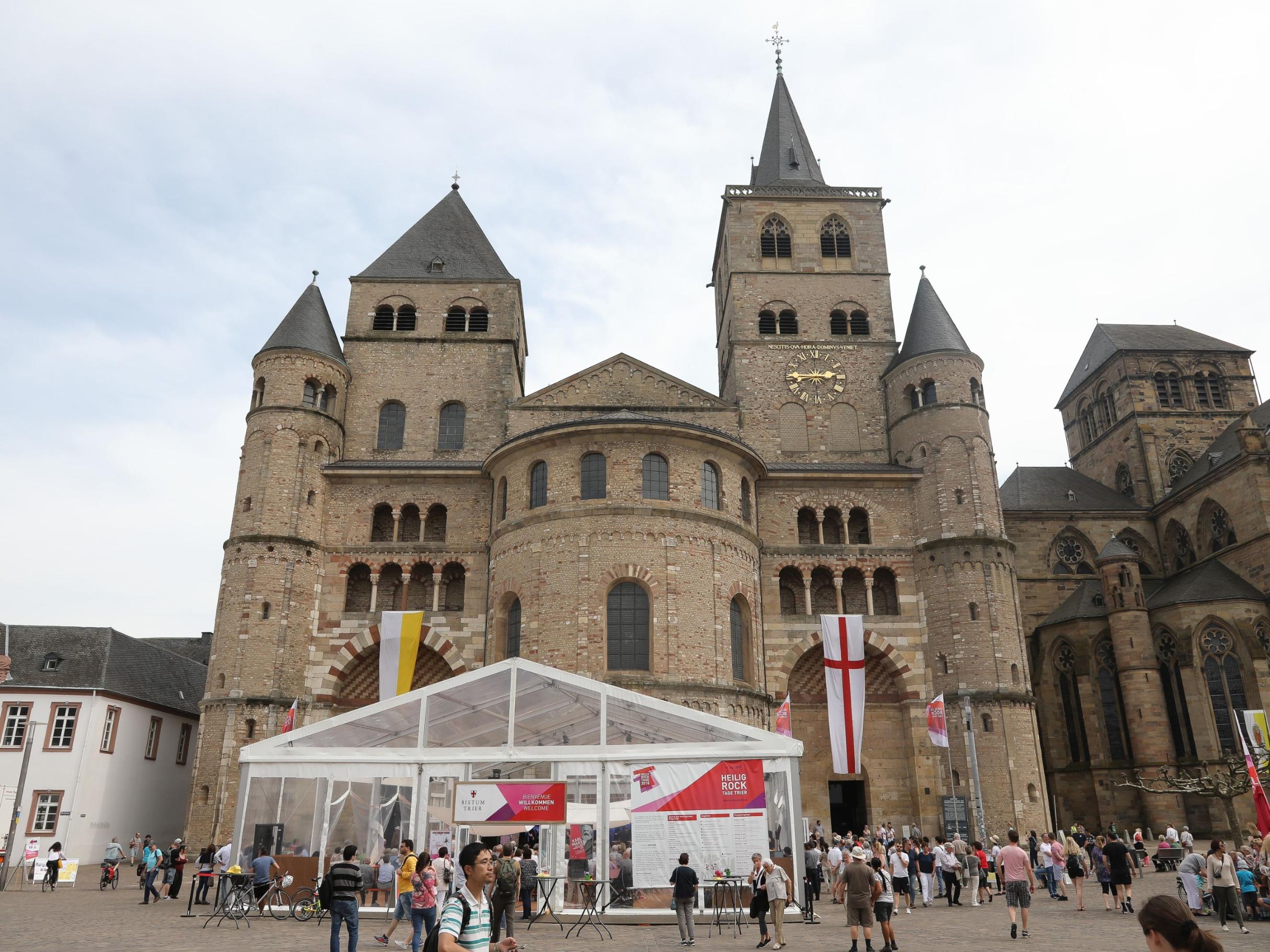 Blick auf den Trierer Dom. Vor dem Dom steht das Festzelt der Heilig-Rock-Tage. Der Dom ist beflaggt. Viele Menschen sind auf dem Domfreihof zu sehen