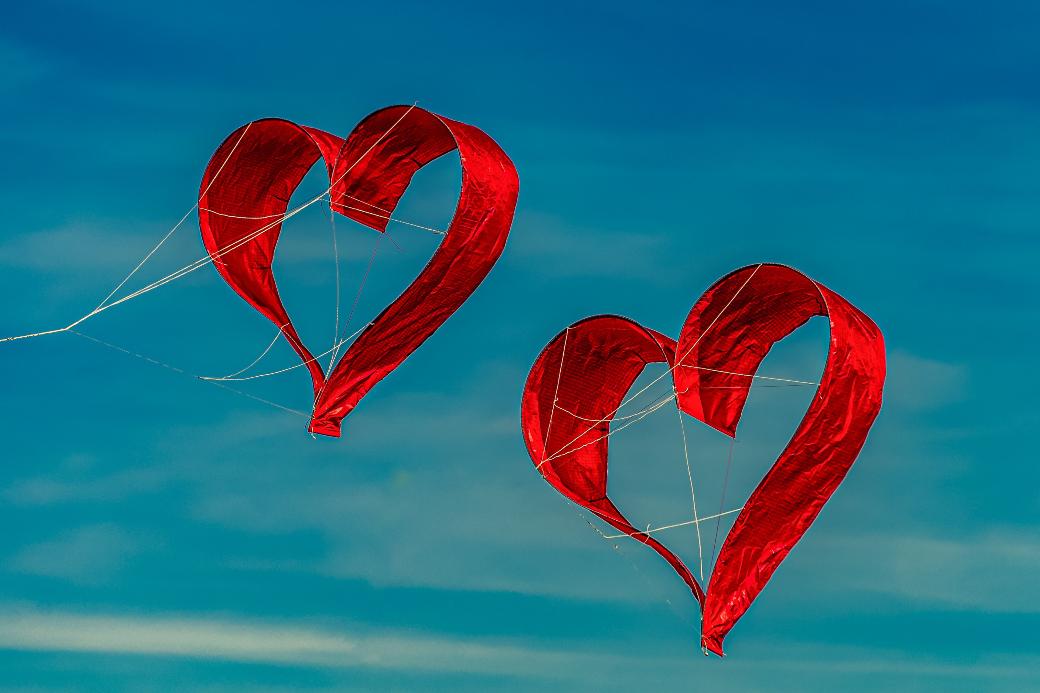 Zwei herzförmige Drachen fliegen vor blauem Himmel