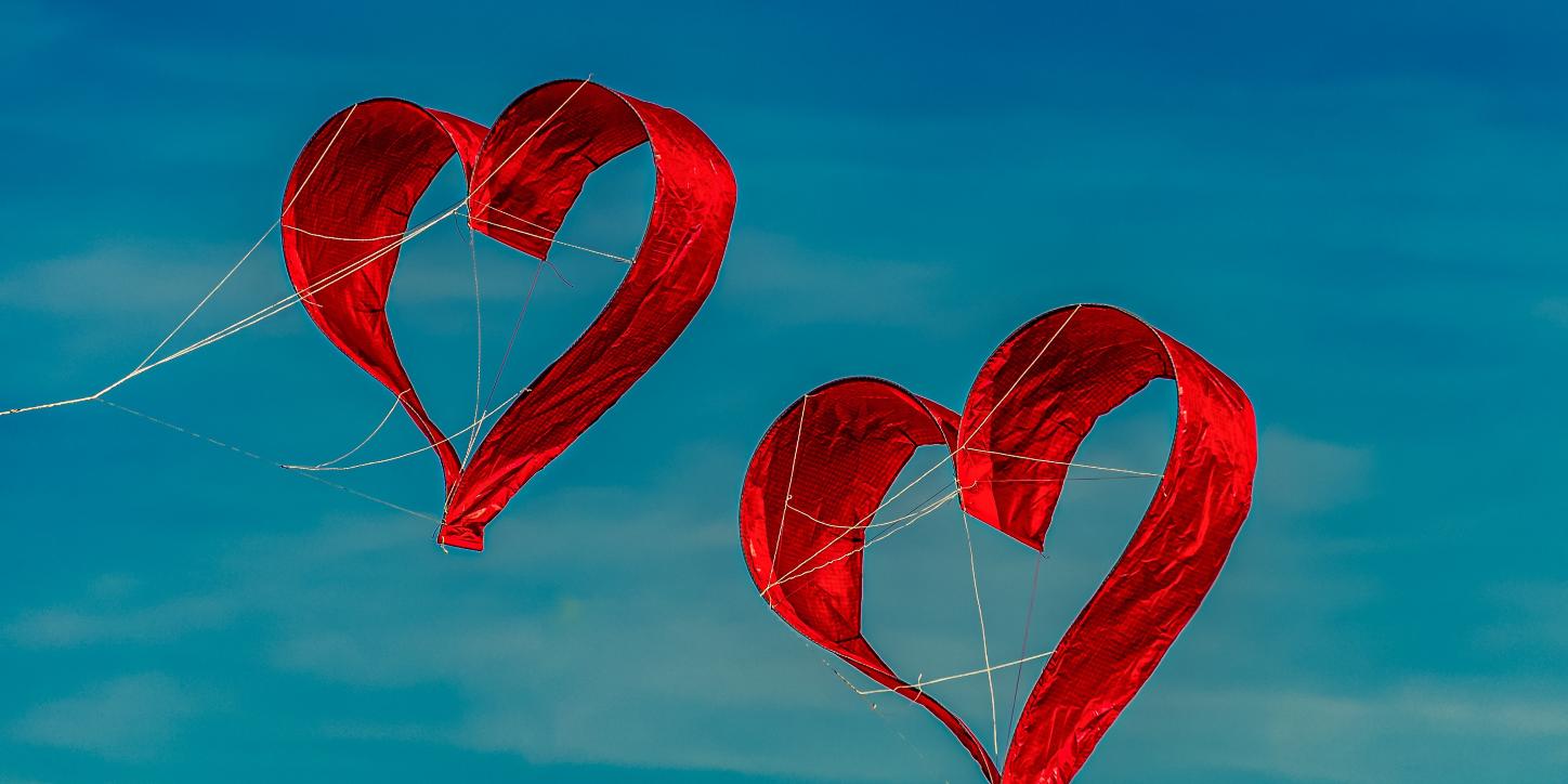 Zwei herzförmige Drachen fliegen vor blauem Himmel
