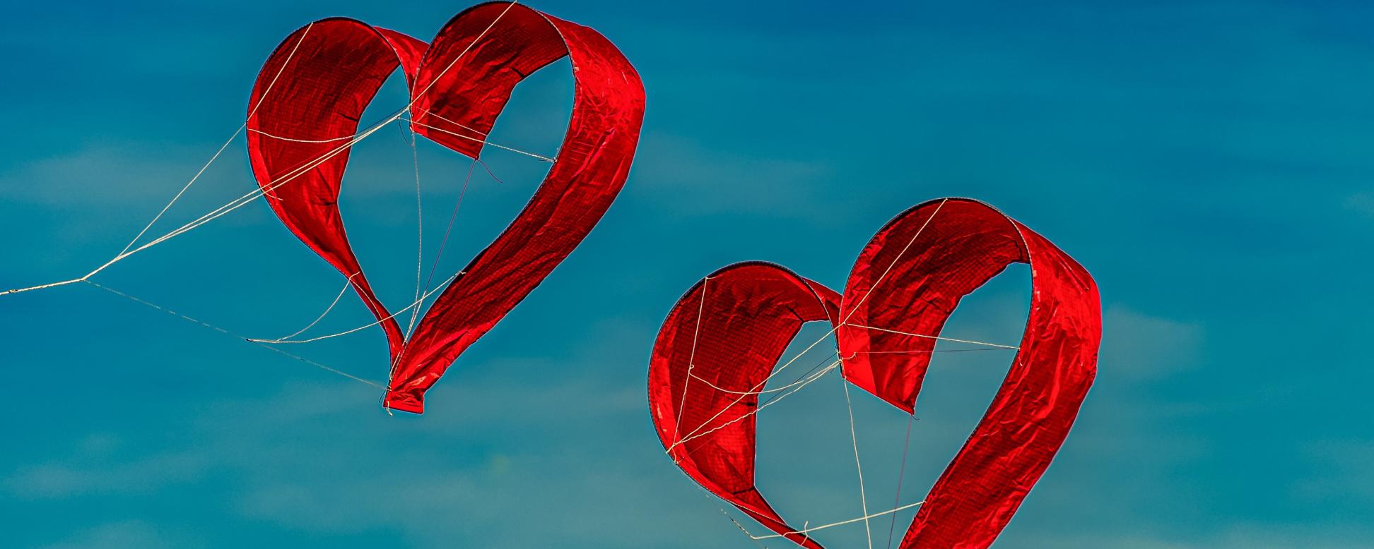 Zwei herzförmige Drachen fliegen vor blauem Himmel