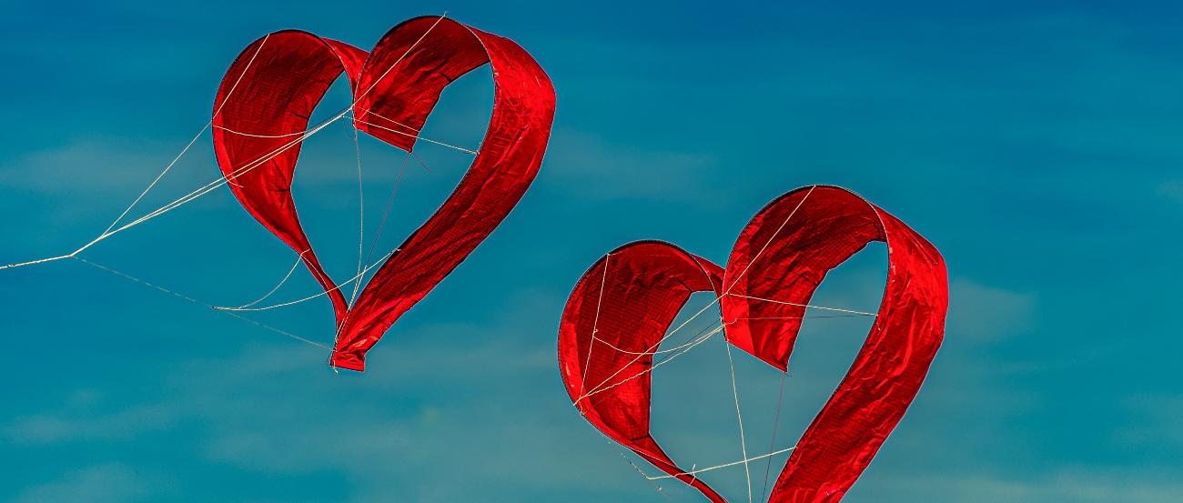 Zwei herzförmige Drachen fliegen vor blauem Himmel