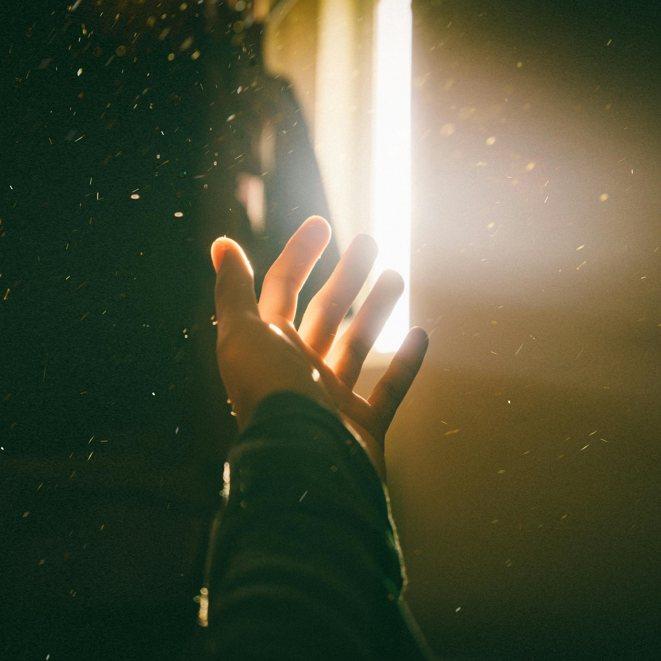 Symbolfoto (c) unsplash.com Eine Hand wird in Richtung Türspalt gestreckt, durch den helles Licht erstrahlt